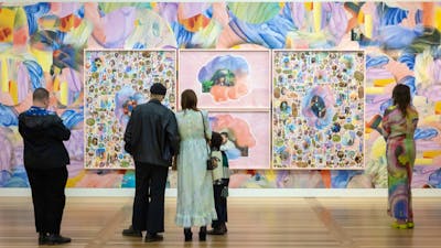 Five people look at a vibrant portrait collage upon a colourful wall.
