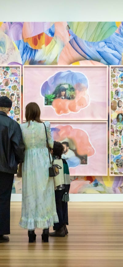 Five people look at a vibrant portrait collage upon a colourful wall.