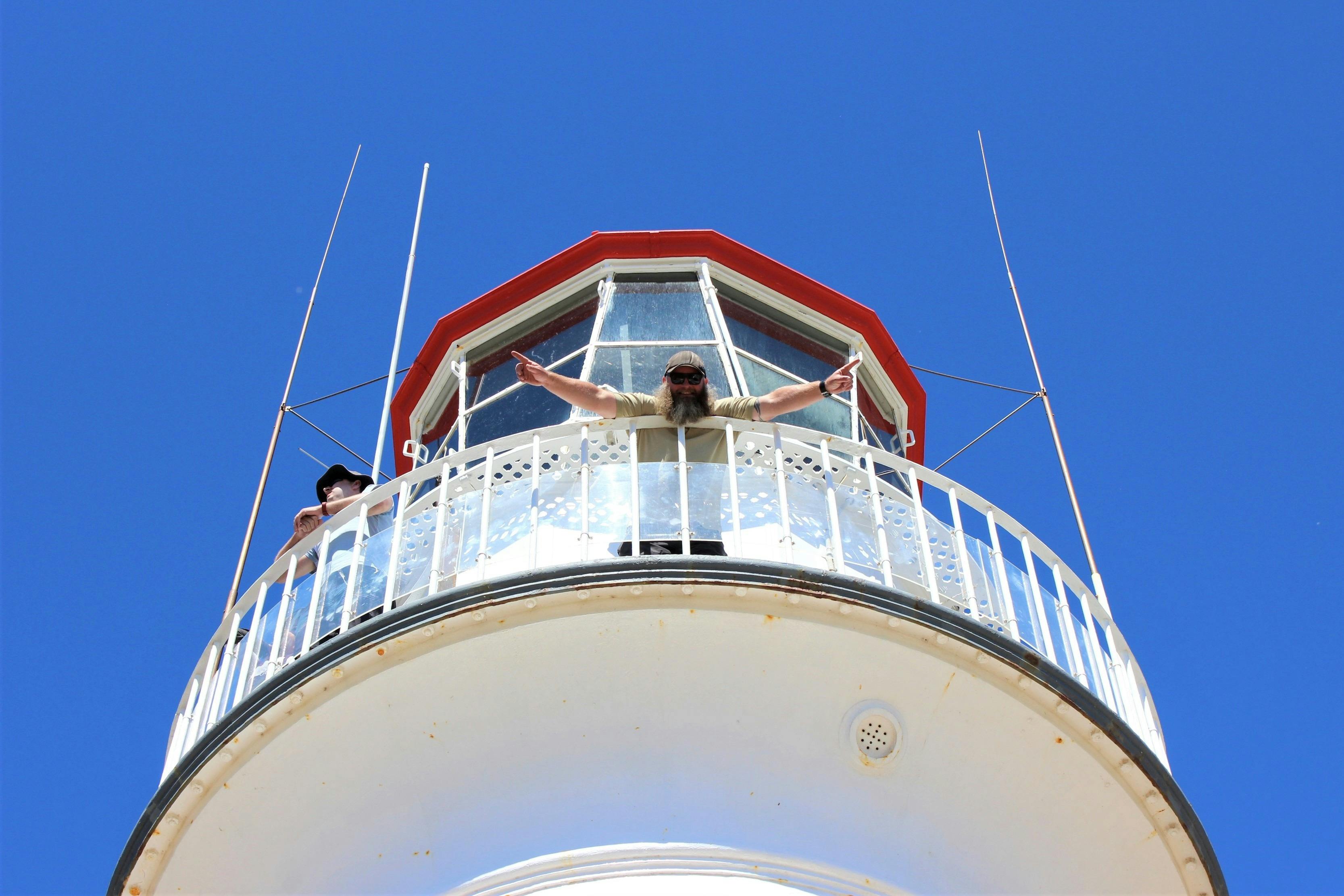 Person standing on elevated lighthouse platform arms wide open waving hello