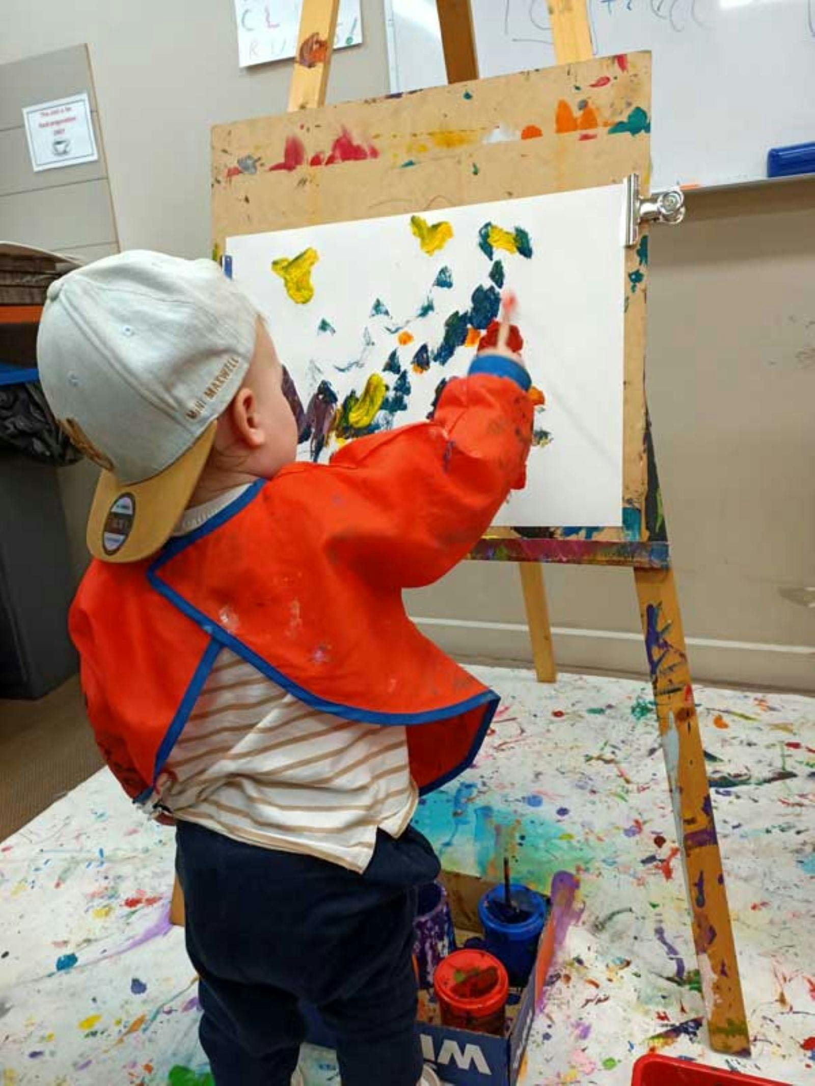 A young child painting on paper resting on an easel.