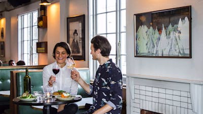 Couple with food and wine on tall stools by a fire place