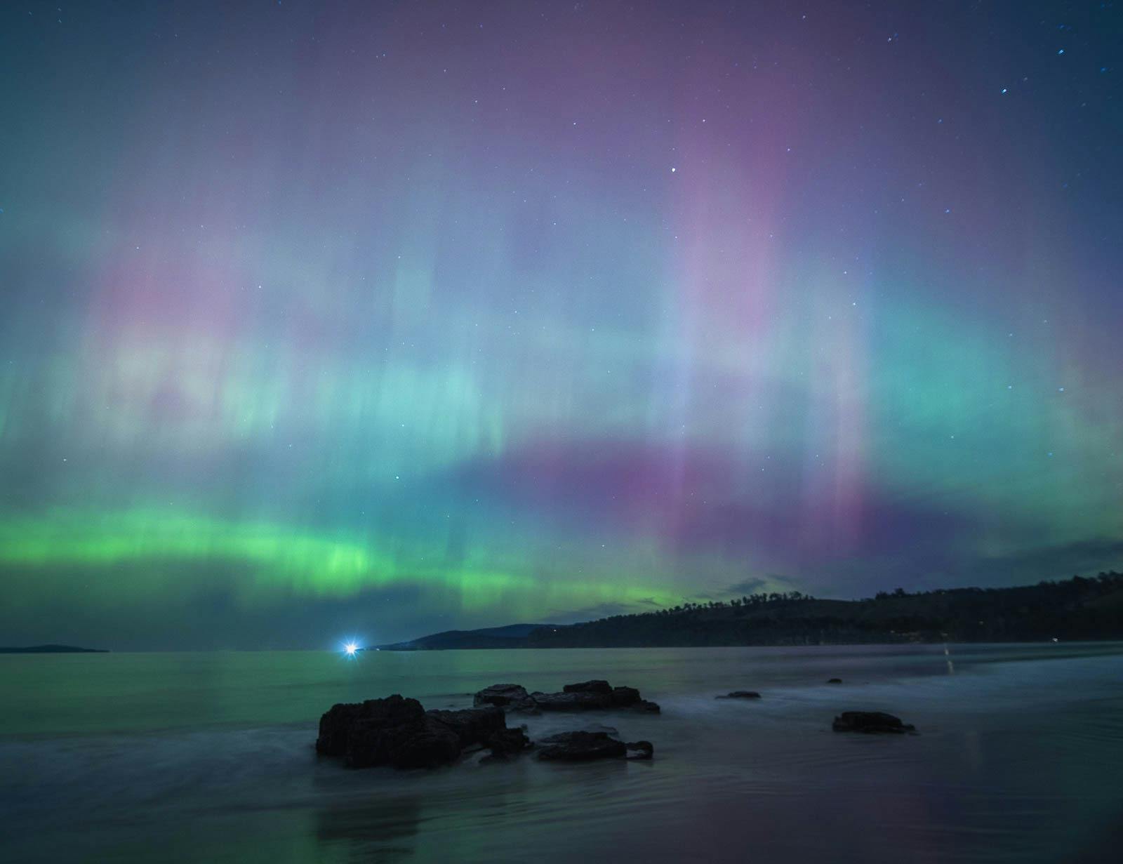 Curtains of pink and green aurora stretching across a star-filled night sky.
