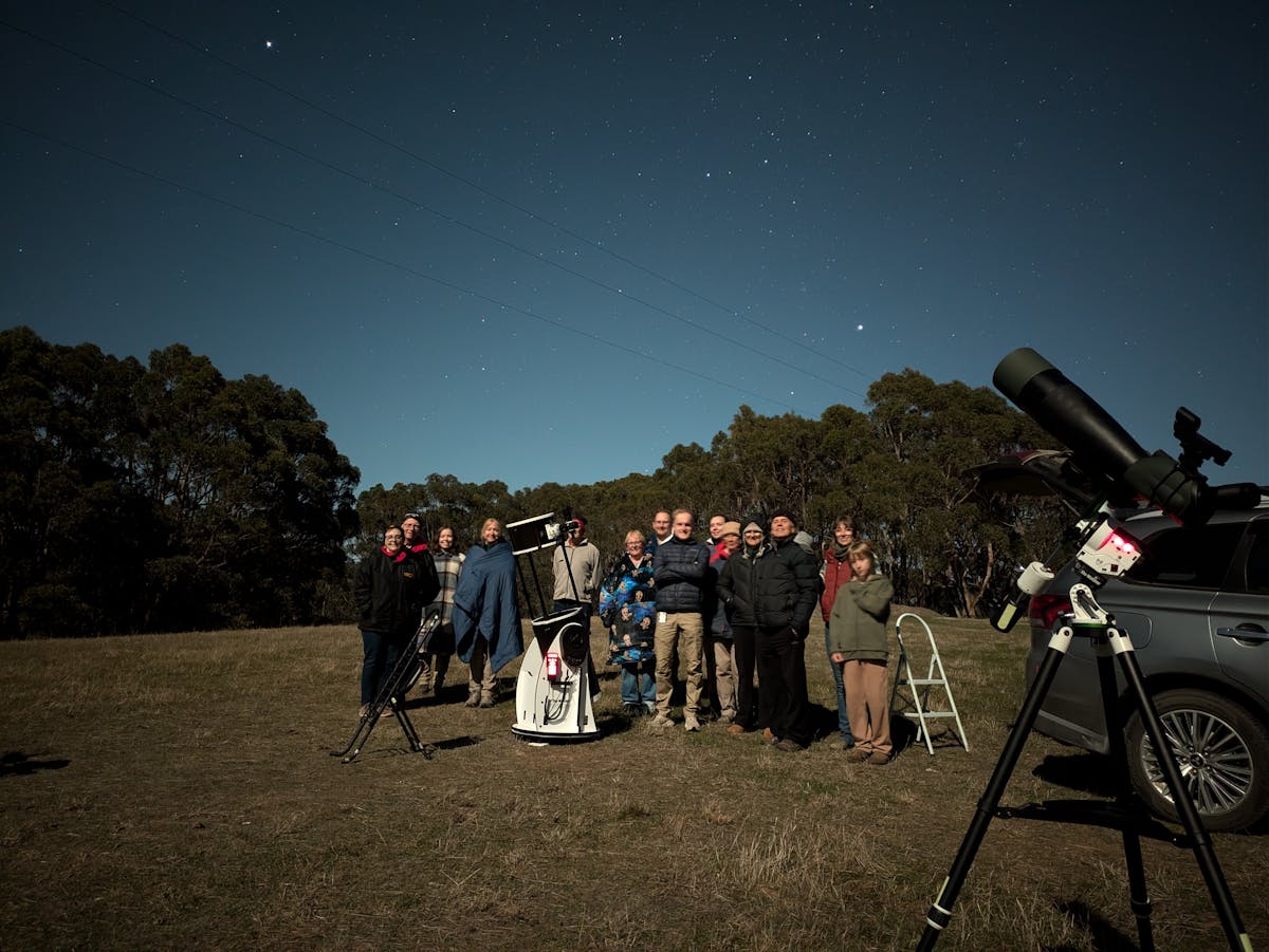 a night sky tour group posing with telescopes, illuminated by a full moon