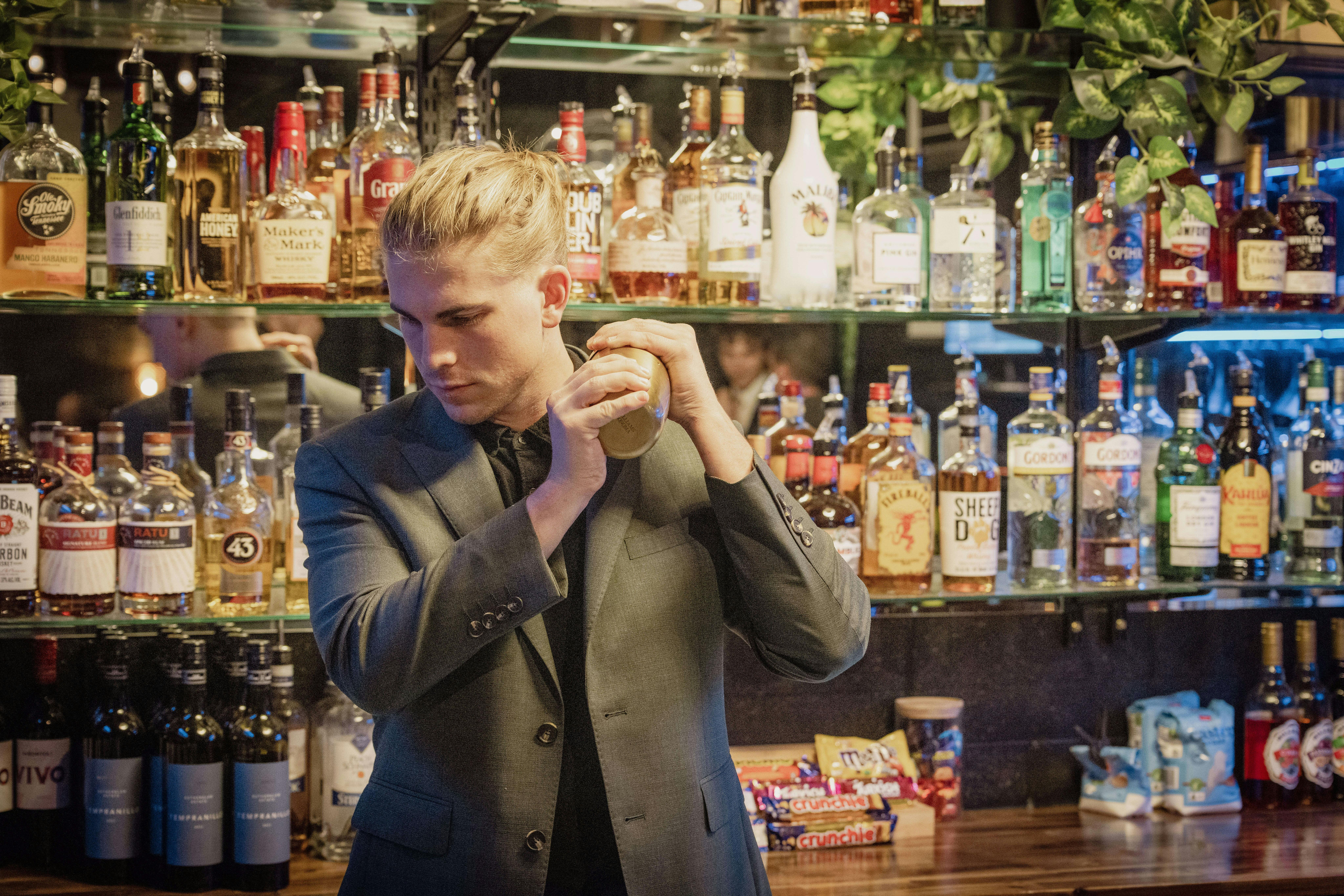 Man behind bar in green suit shakes cocktail in Club Noir