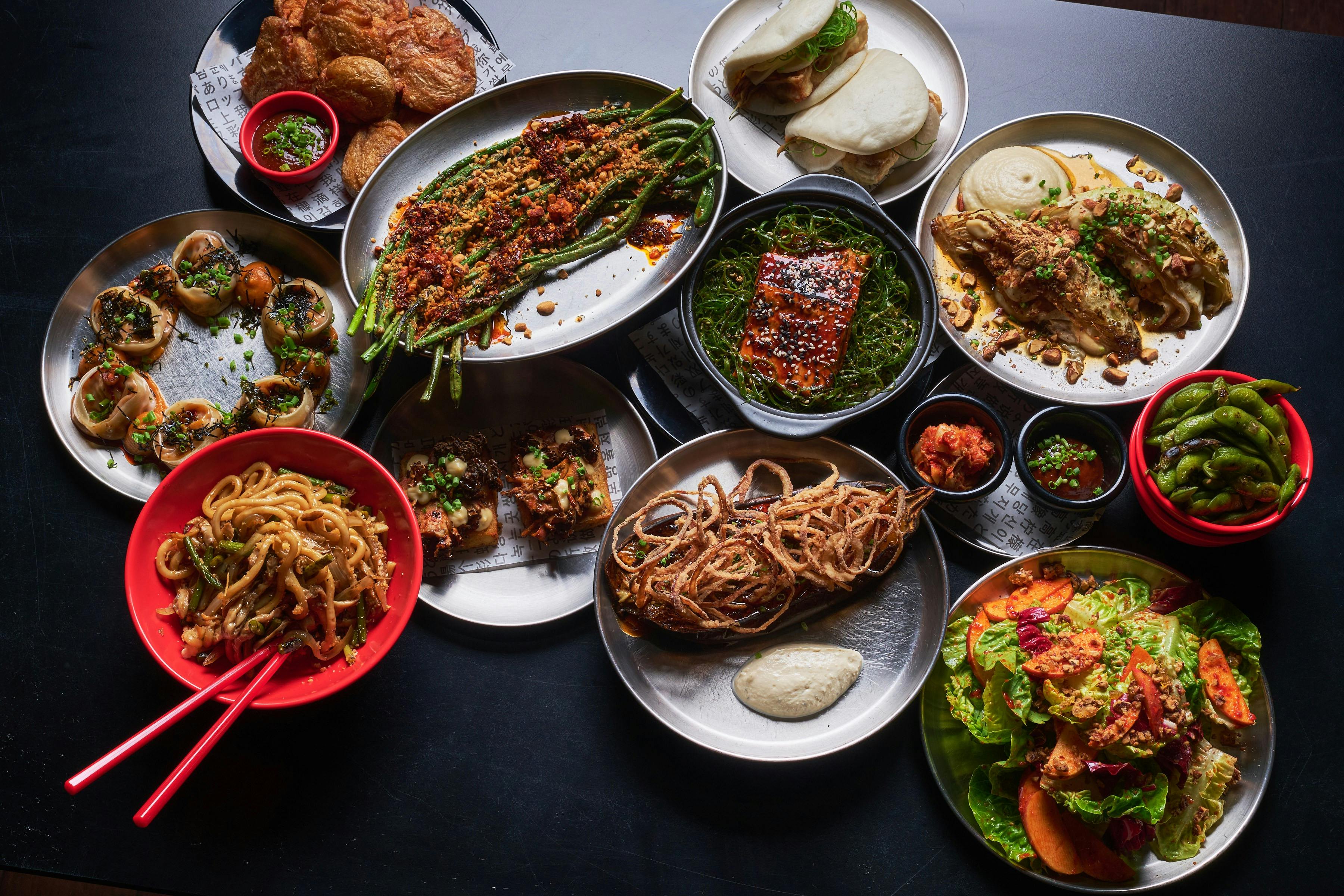 A flat lay photo of vegan dishes including roasted eggplant, bass and noodles.