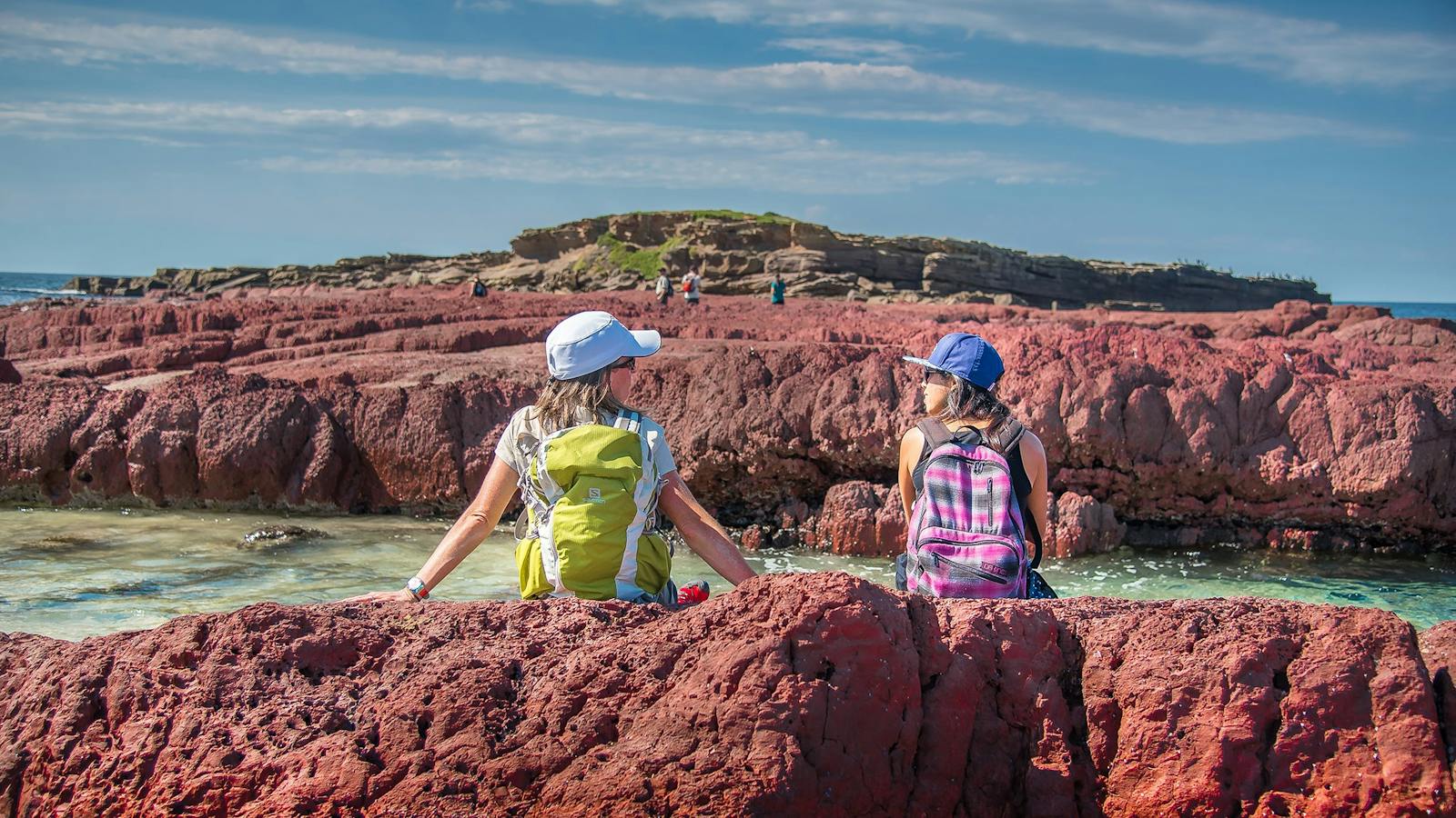 Two women sitting on rocks near ocean