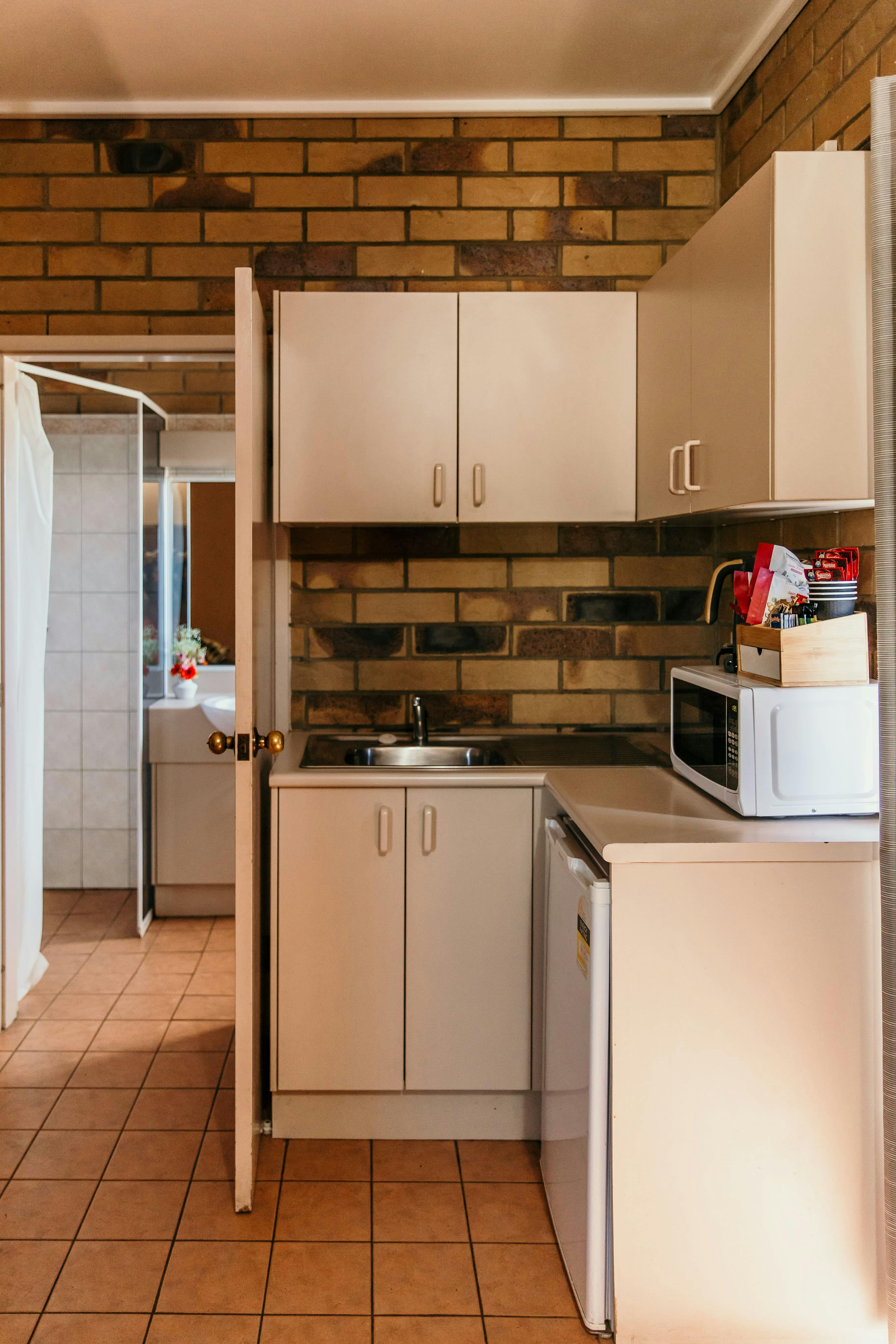 Kitchenette with sink, cupboards, microwave and an open door that leads to a bathroom.