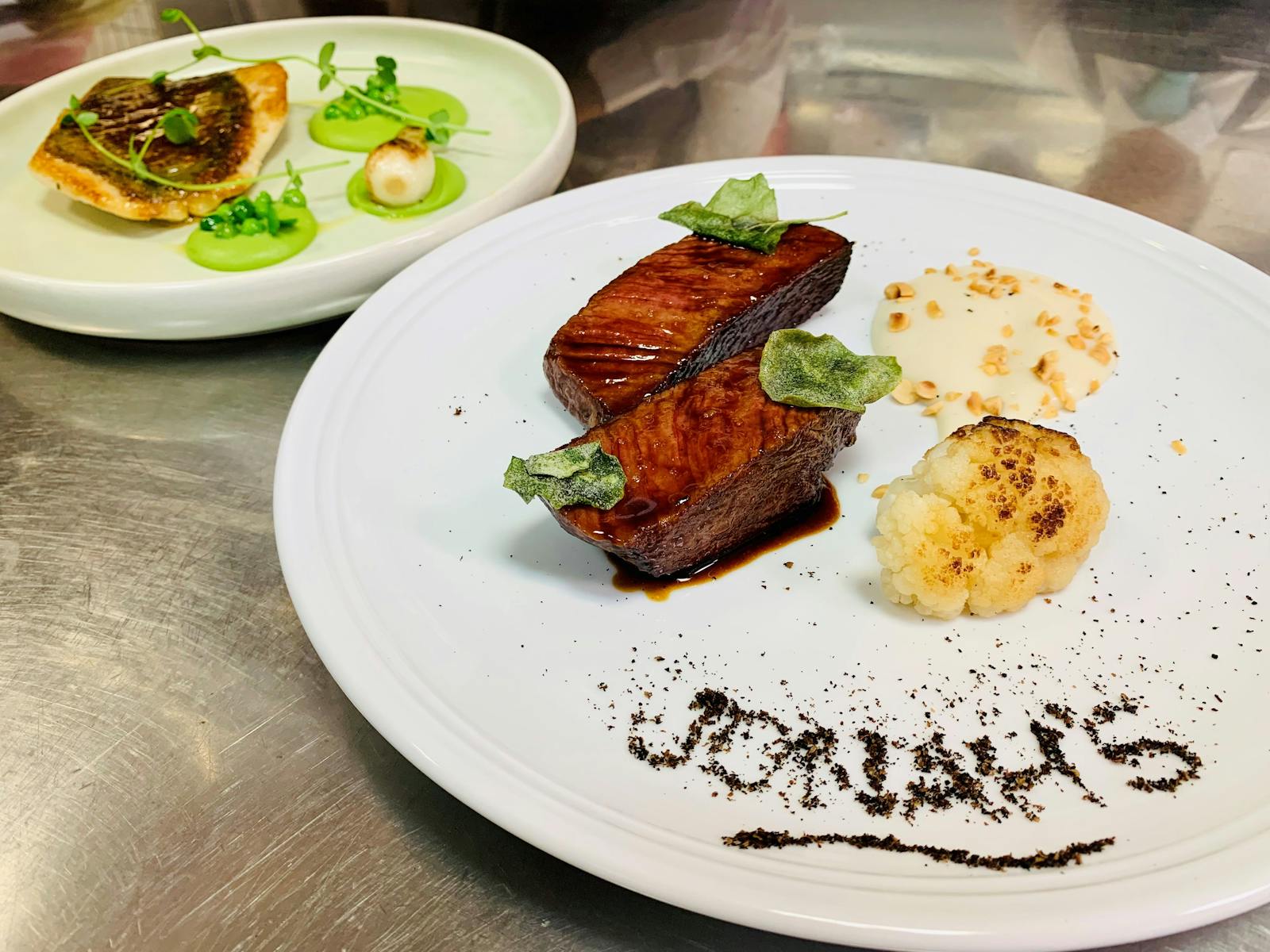 ジューシーな和牛と、皿に胡椒で「Jonah's」と書かれたもの。後ろには天然の魚料理が飾られている。