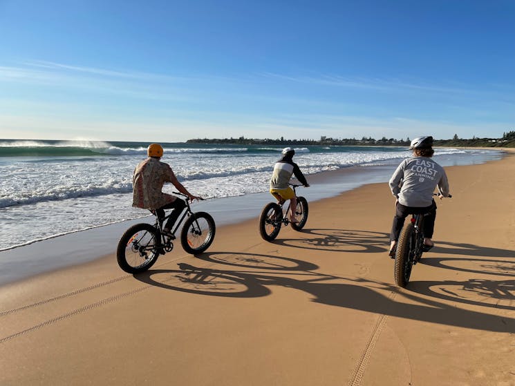 Three people riding bikes on the sand.