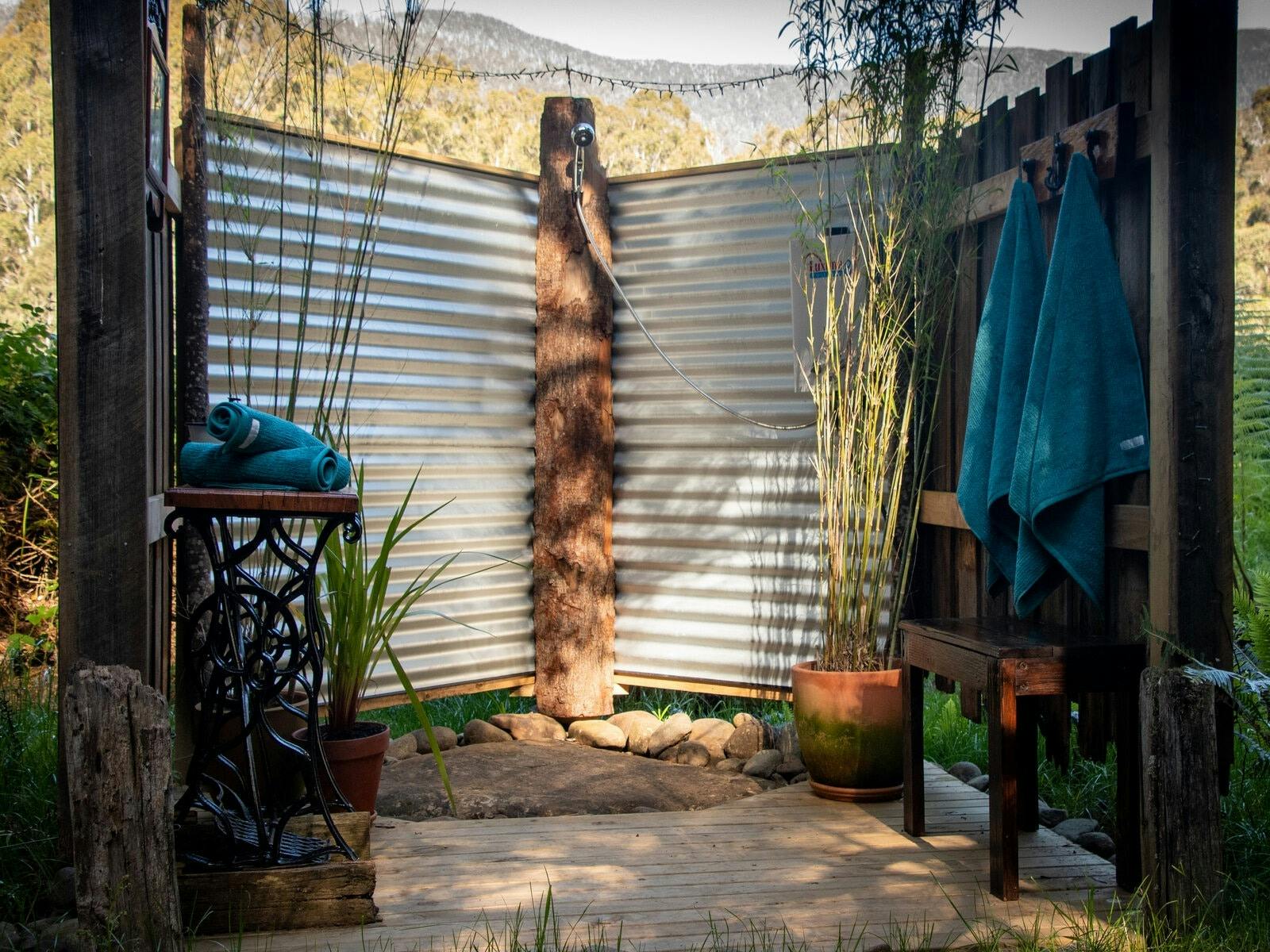 An outdoor shower space made from timber and iron with tall bamboo plants and wooden benches.
