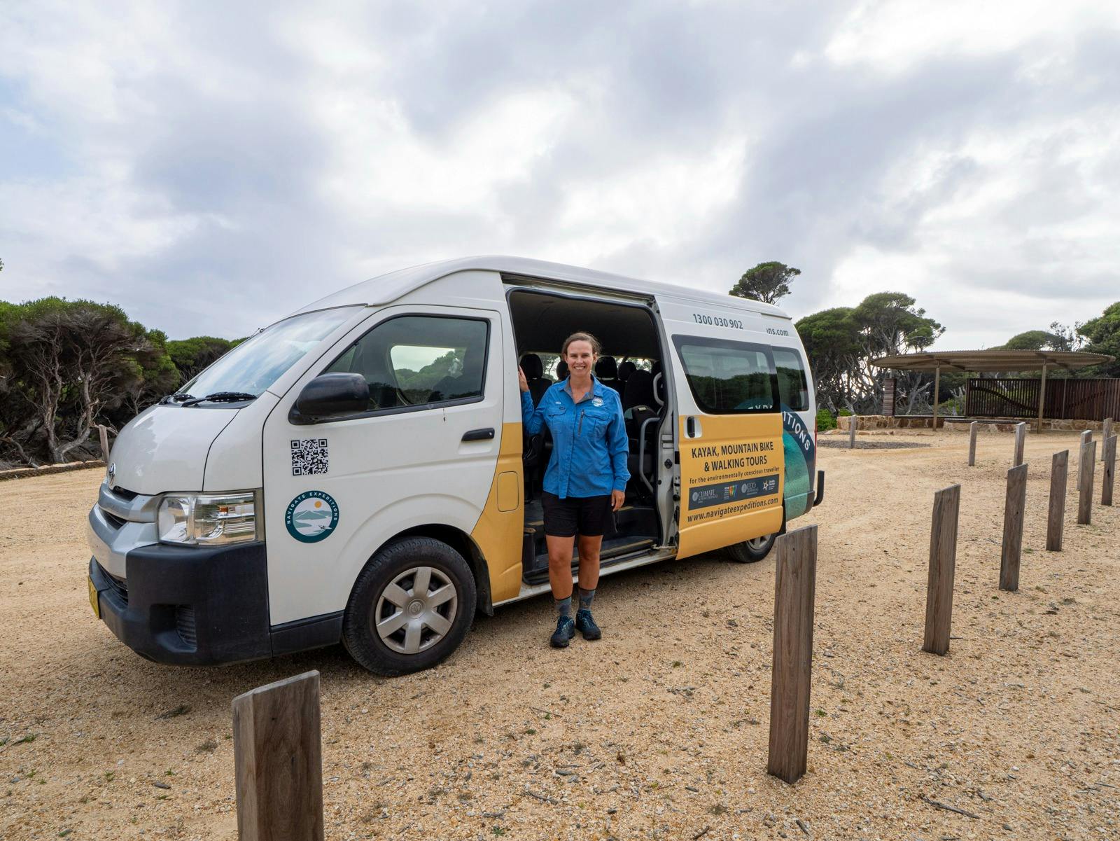 A driver in uniform stands next to a transfer mini-bus, with the bus door open.