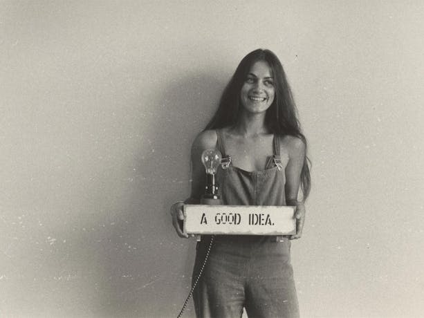 A young woman with long hair holding a sign that says 'A Good Idea' with a lightbulb on top of it.