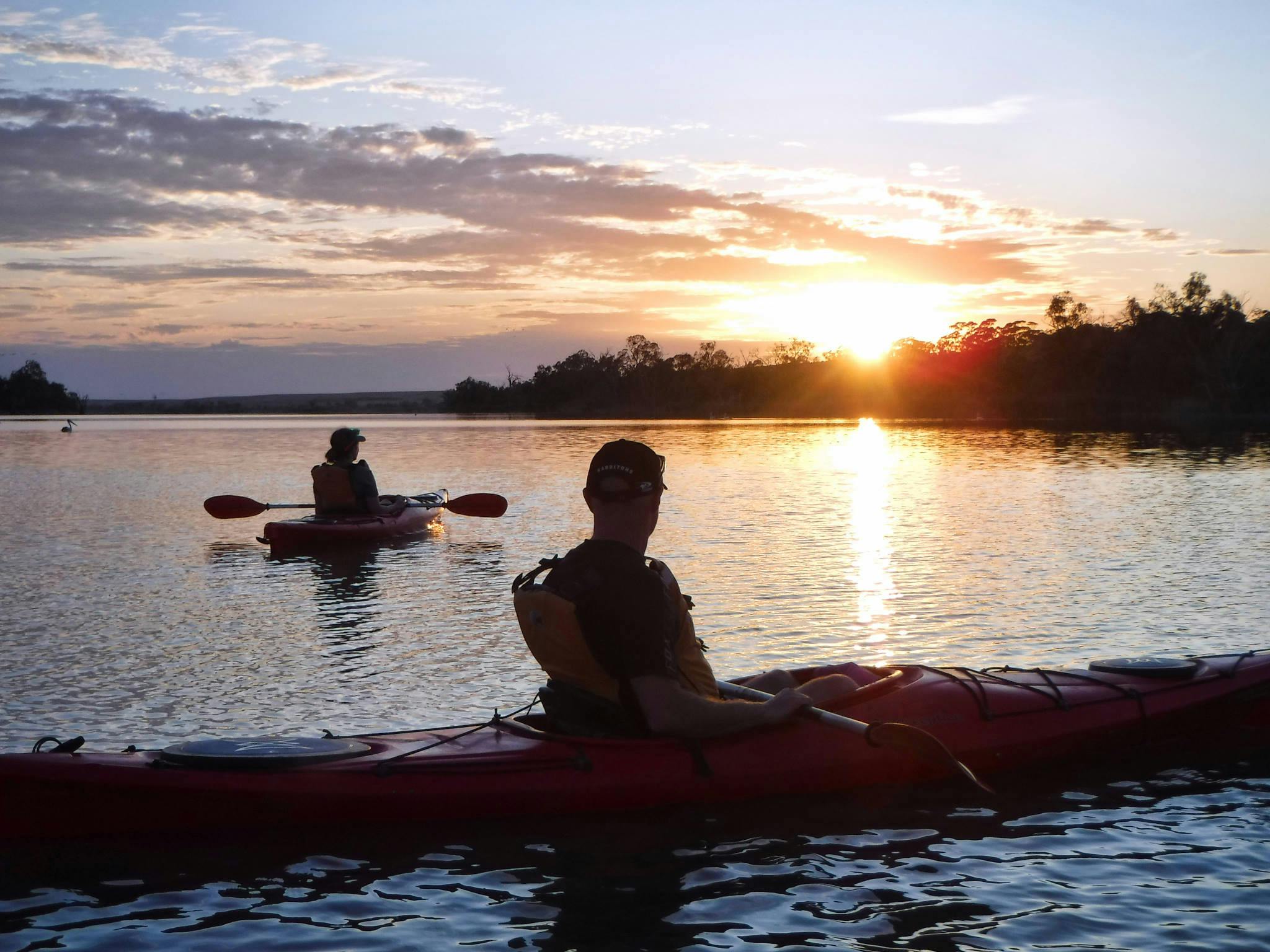 Kayakers watch a colourful sunrise over a lake.