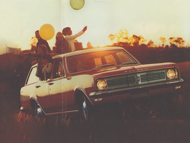 A Holden Kingswood car parked  on a grassy field at sunset with children hanging out of the windows