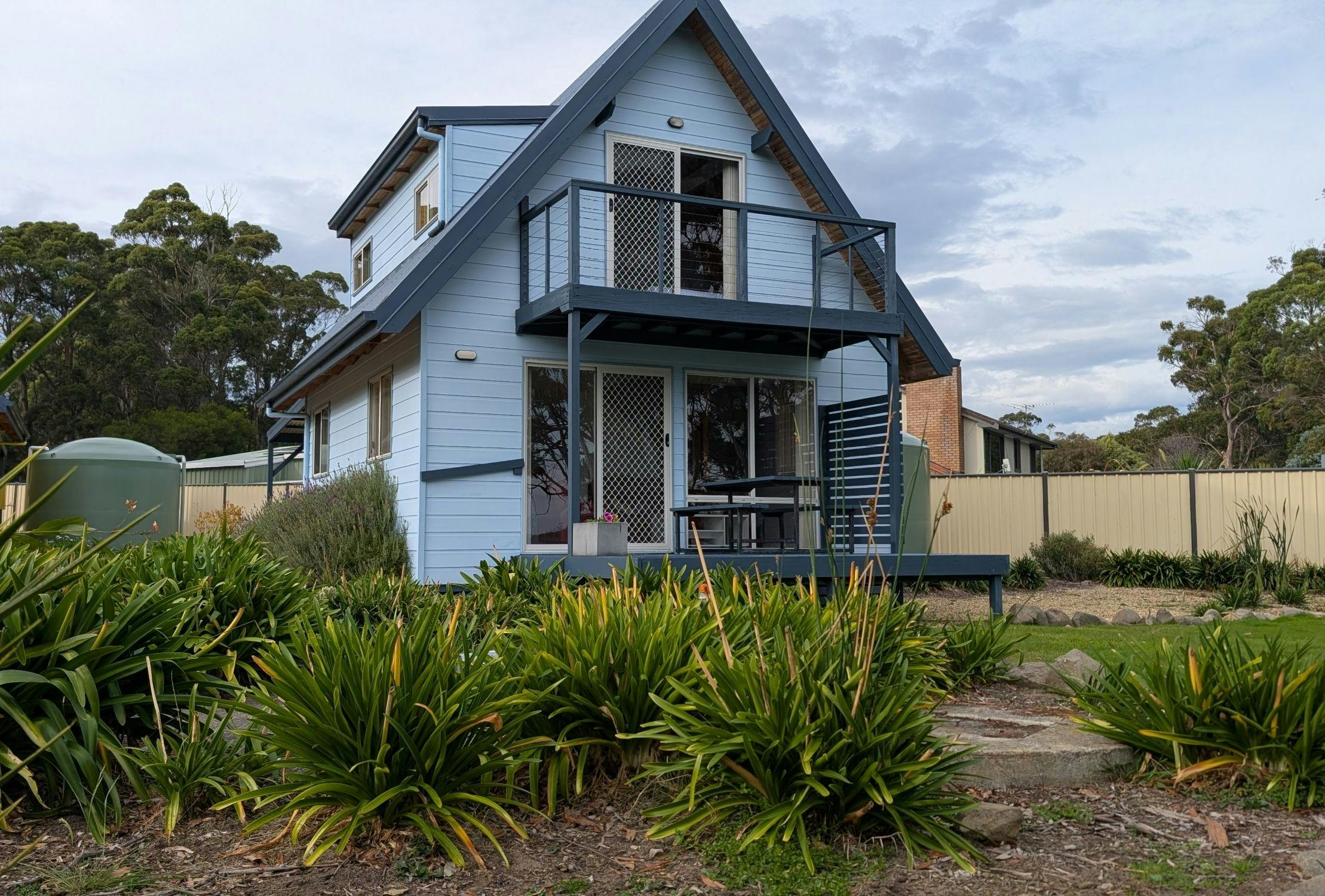 Two-storey blue villa with balcony, deck and garden path in a coastal setting.