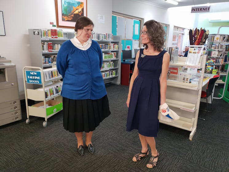 Two women standing in a library dressed in 1950s era clothing