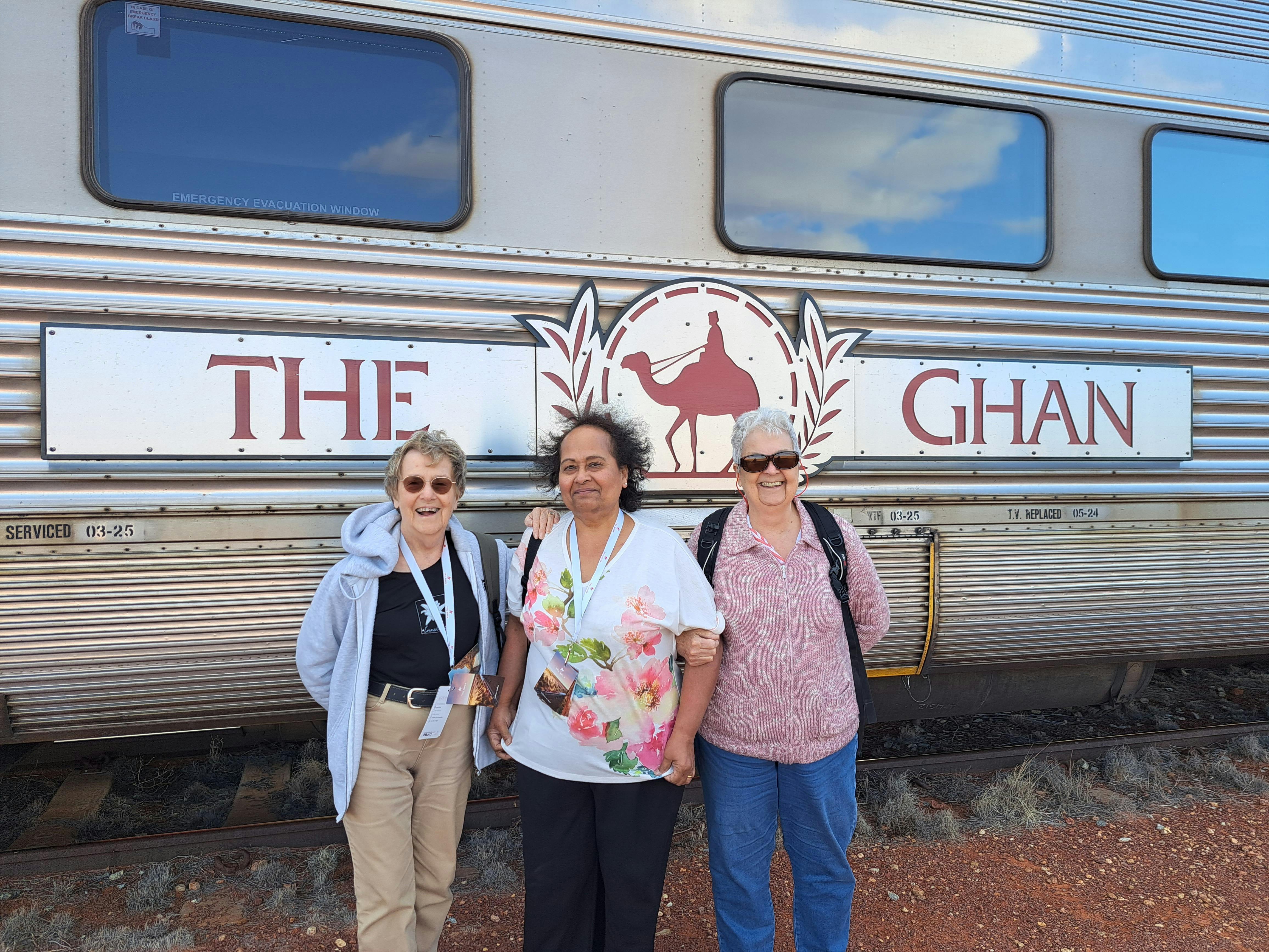 three senior ladies infront of a train carriage and the ghan sign