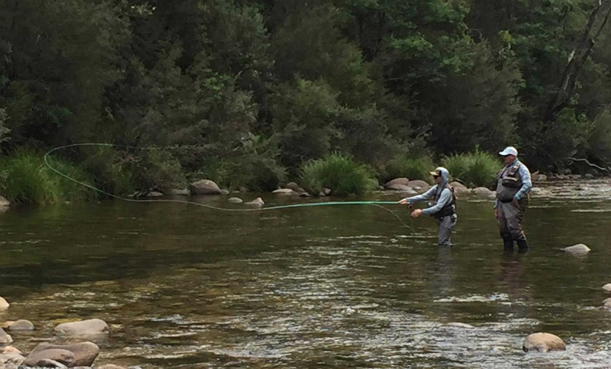 A fishing guide standing in the river behind a client casting a fly fishing rod