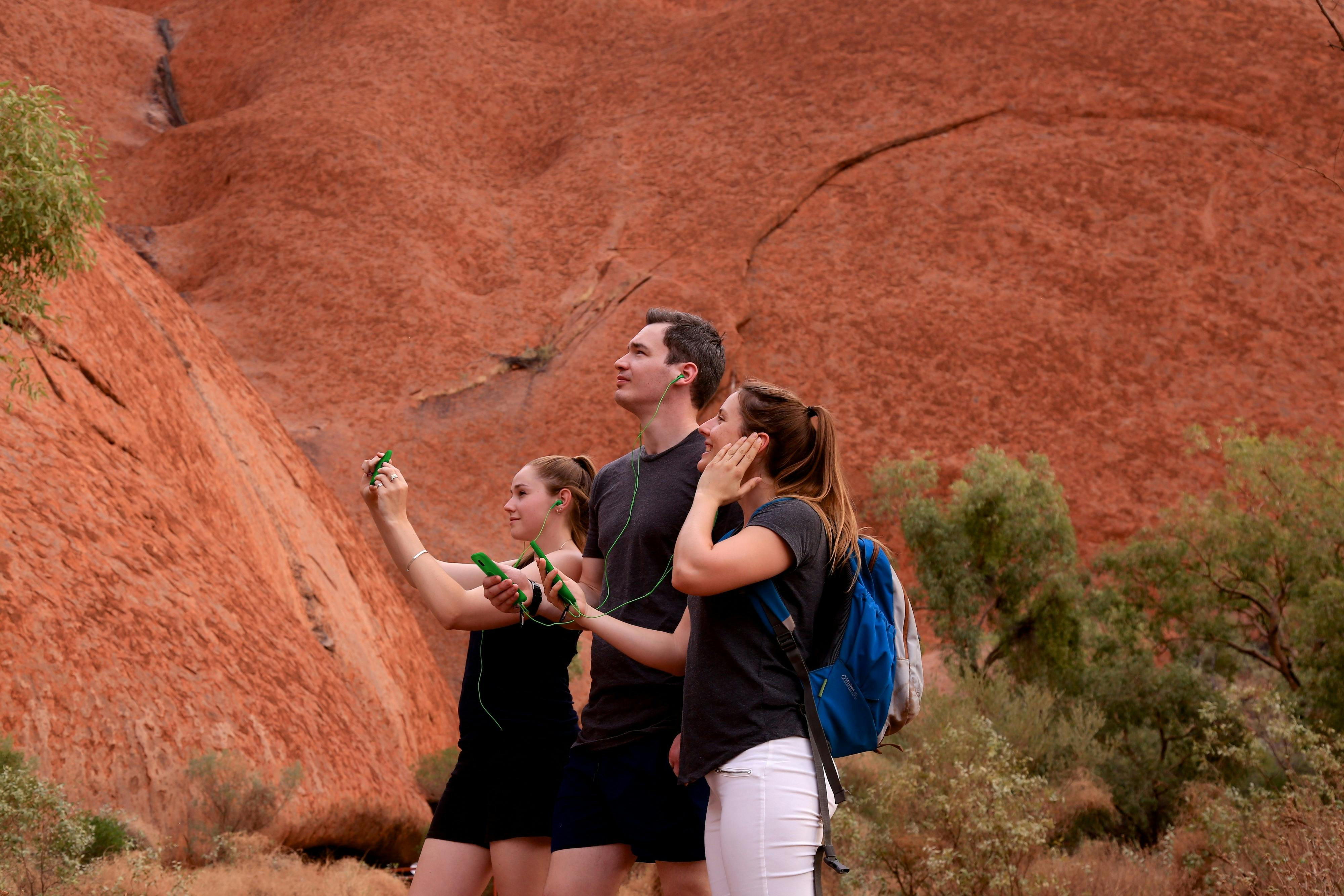 A group of friends look up at Uluru, entranced by the stories their audio guide is telling them.