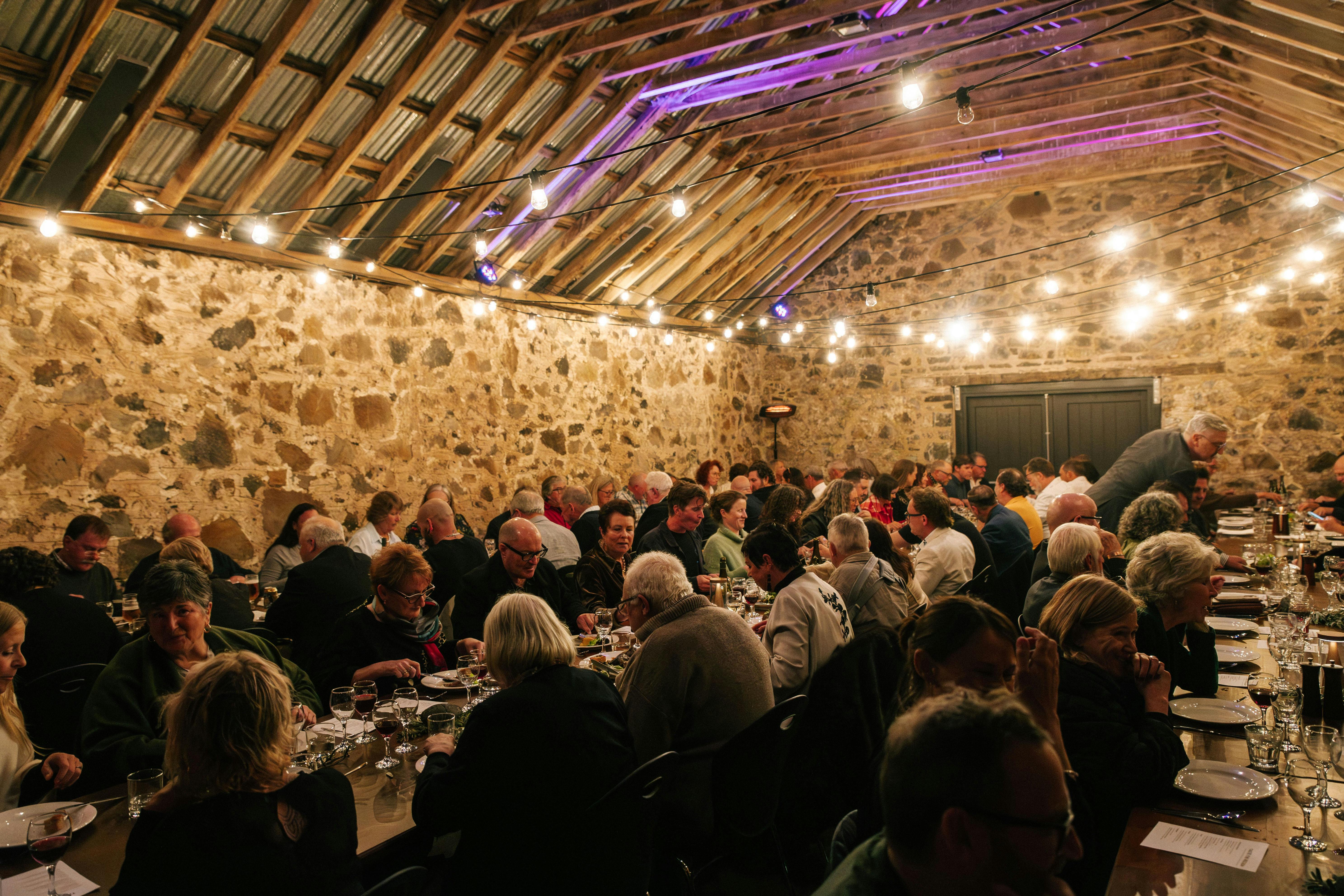 Old barnroom, people on log tables eating, fairy lights