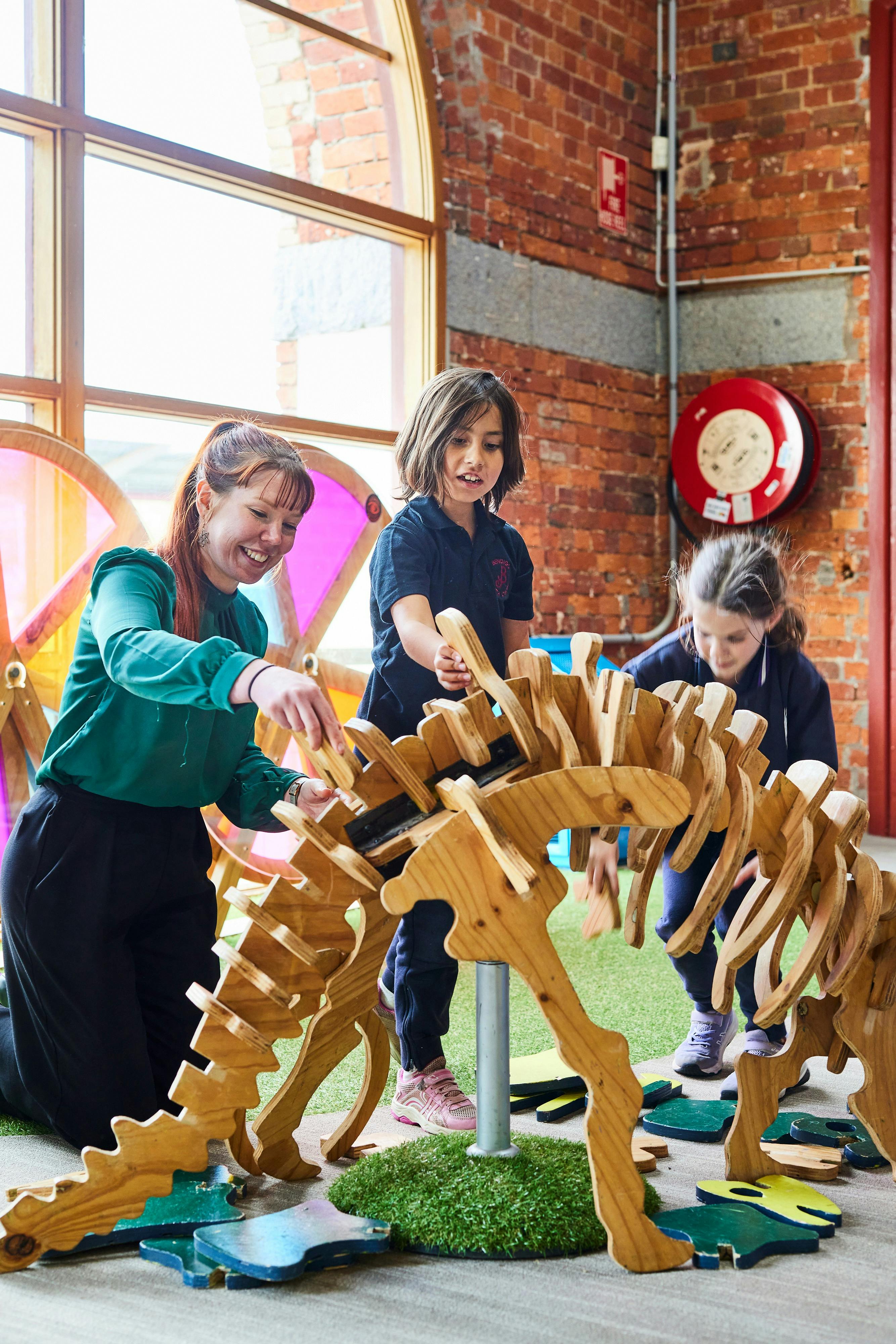 Adult and 2 primary school aged children building a wooden dinosaur