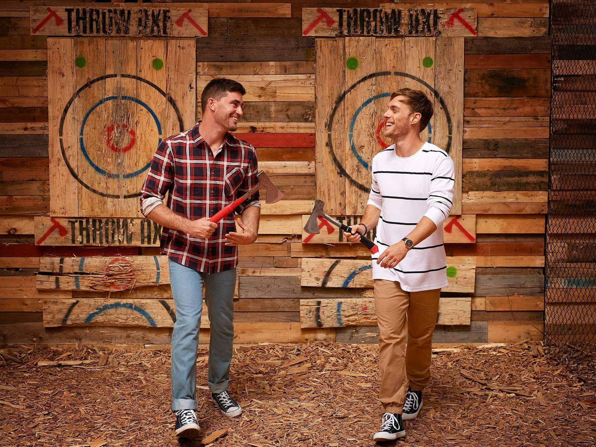 Two guys laughing carrying axes in front of Throw Axe targets
