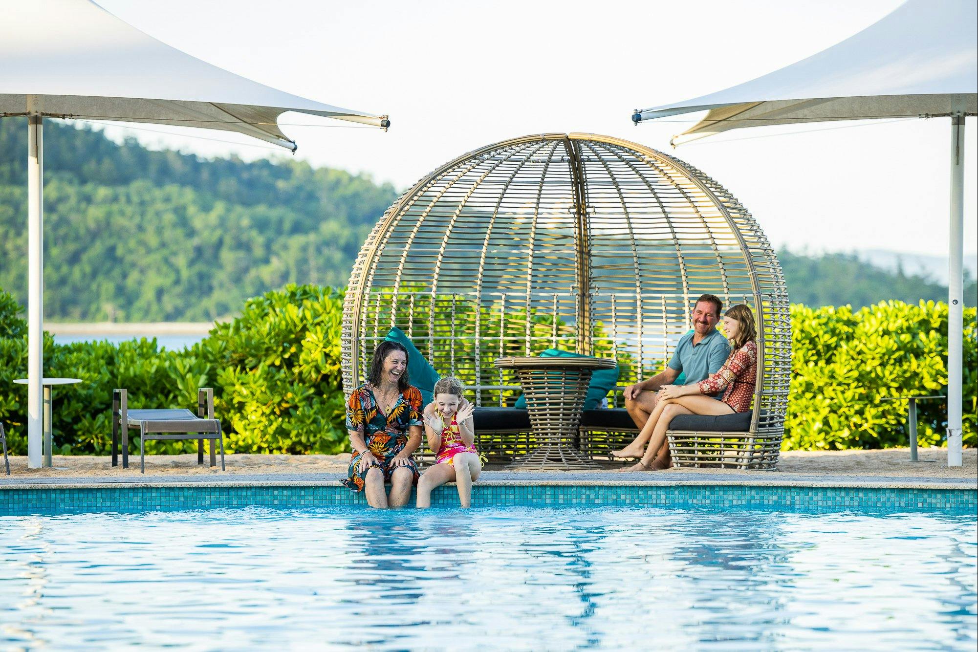 Young family of four smiling in the main pool area on Daydream Island.