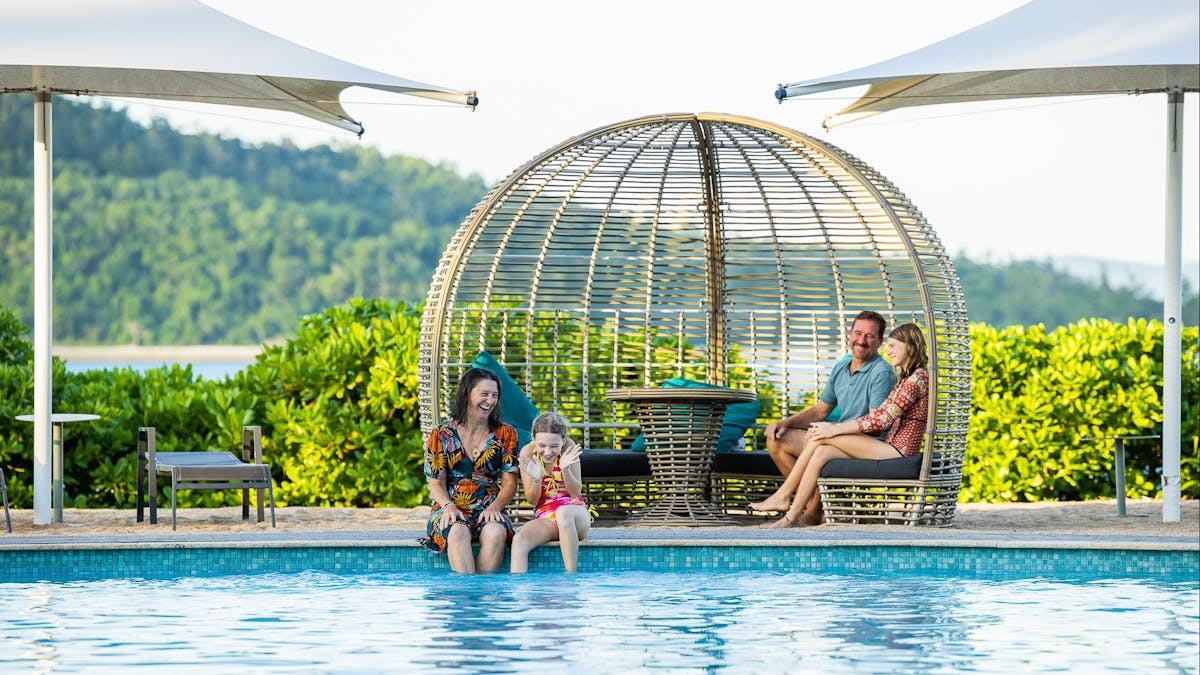 Young family of four smiling in the main pool area on Daydream Island.