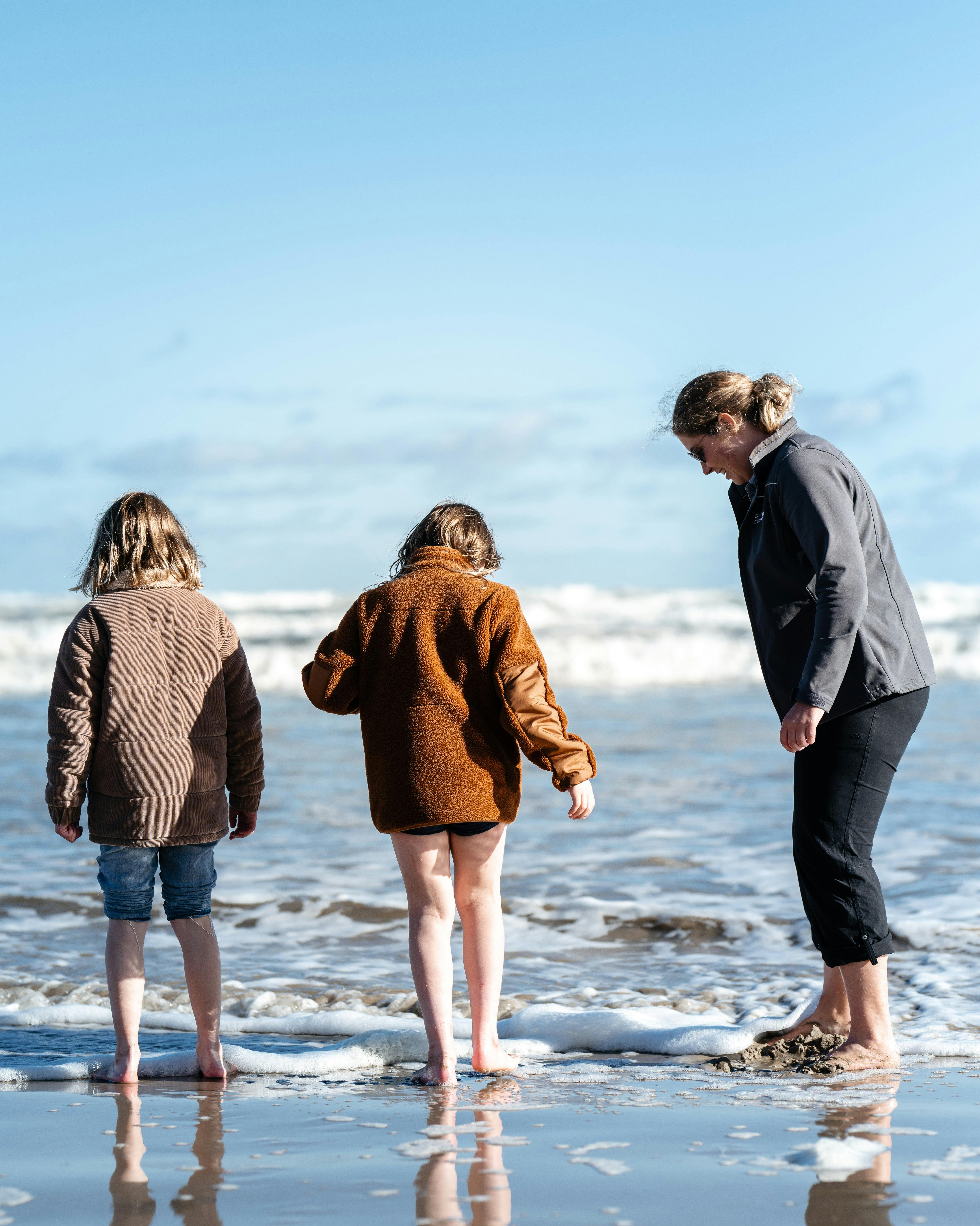 Two Children and guide digging for pipi using their feet in the tide of 90 Mile Beach