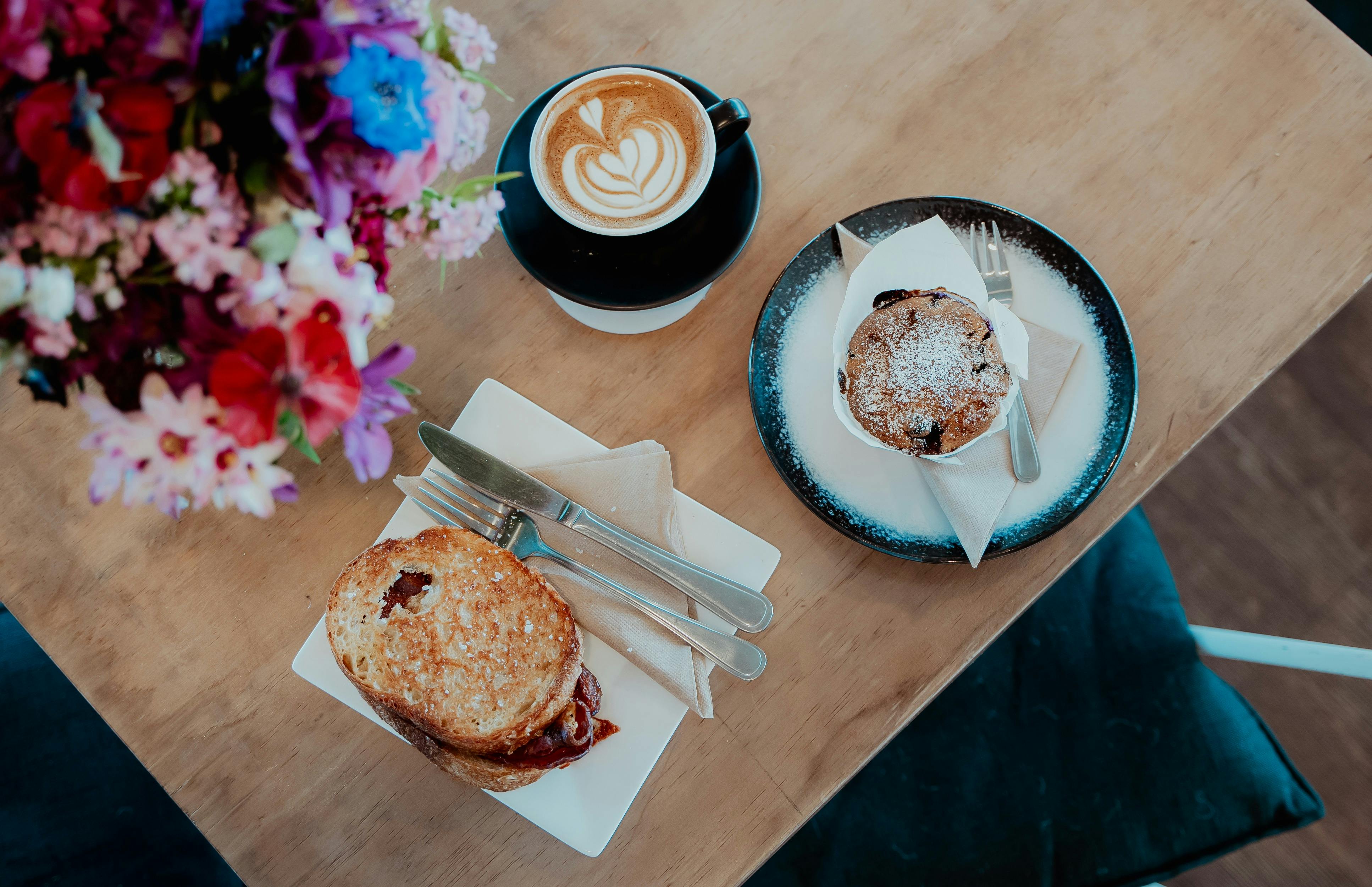A coffee, a toastie and a sweet treat on a cafe table with flowers