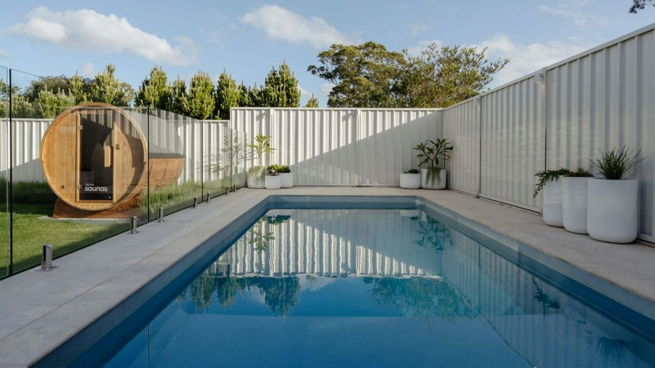 Image of heated pool in backyard with barrel sauna to the left.