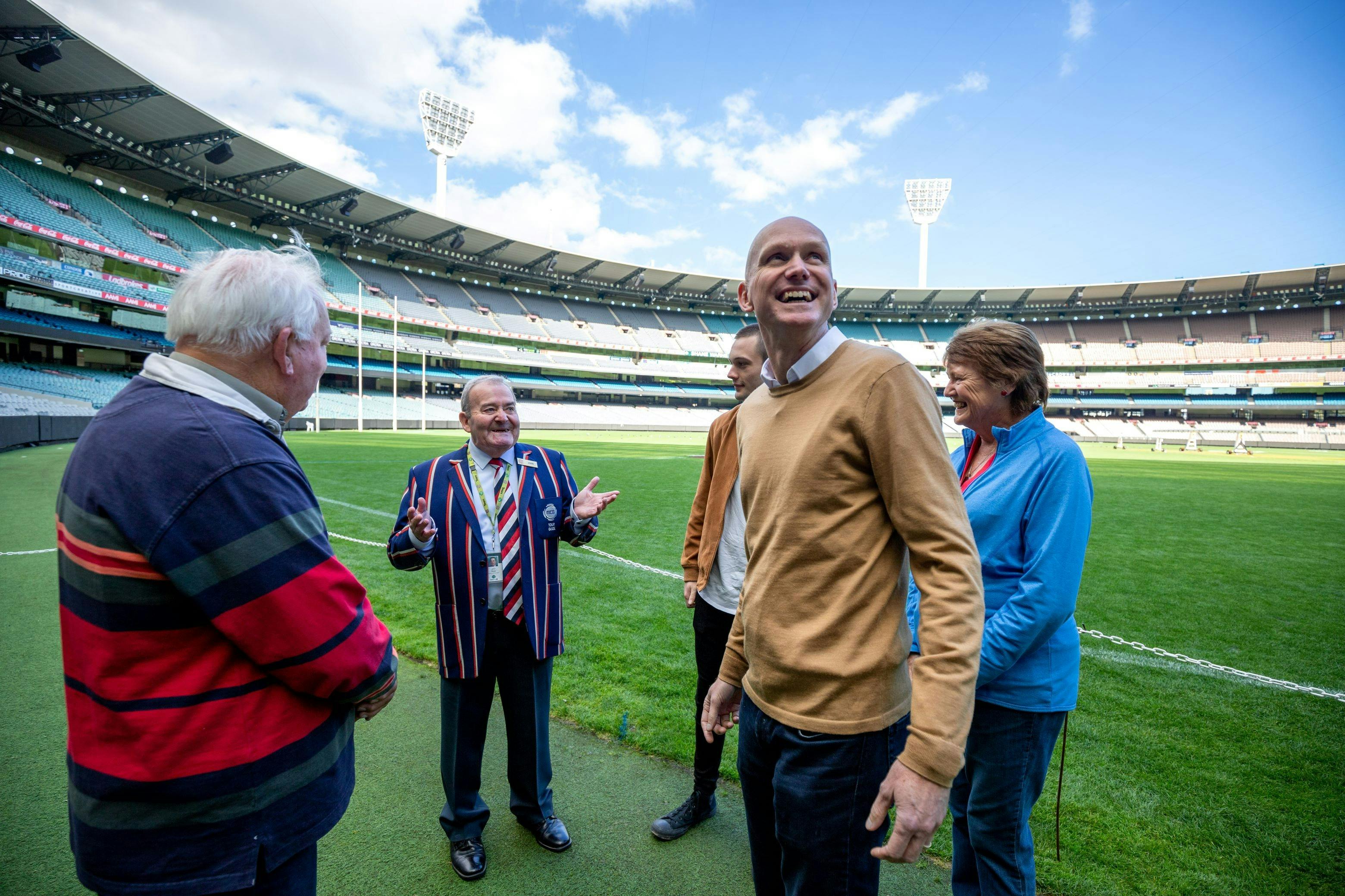 A man is looking up into the distance on a sporting field.  Three people are listening to a guide.