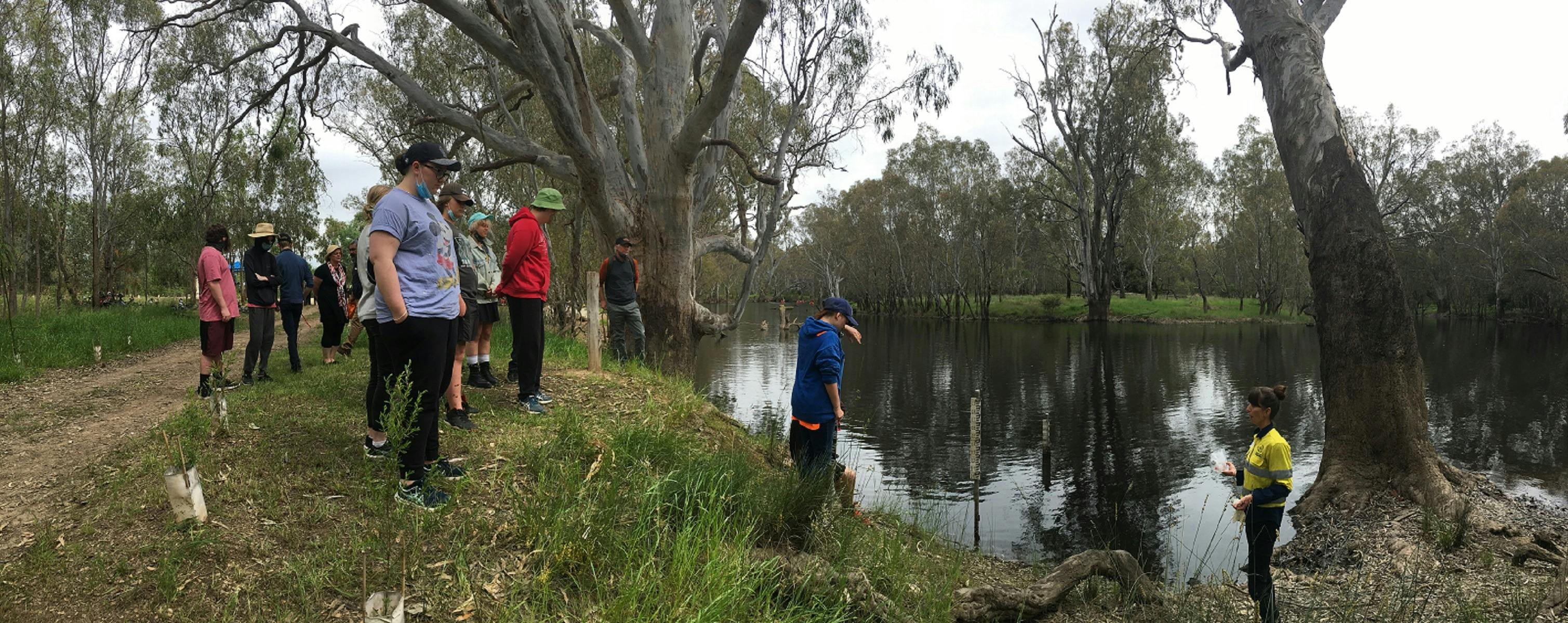 Woman  talking to group  beside billabong, reflections of trees in water, gum trees, grasses,