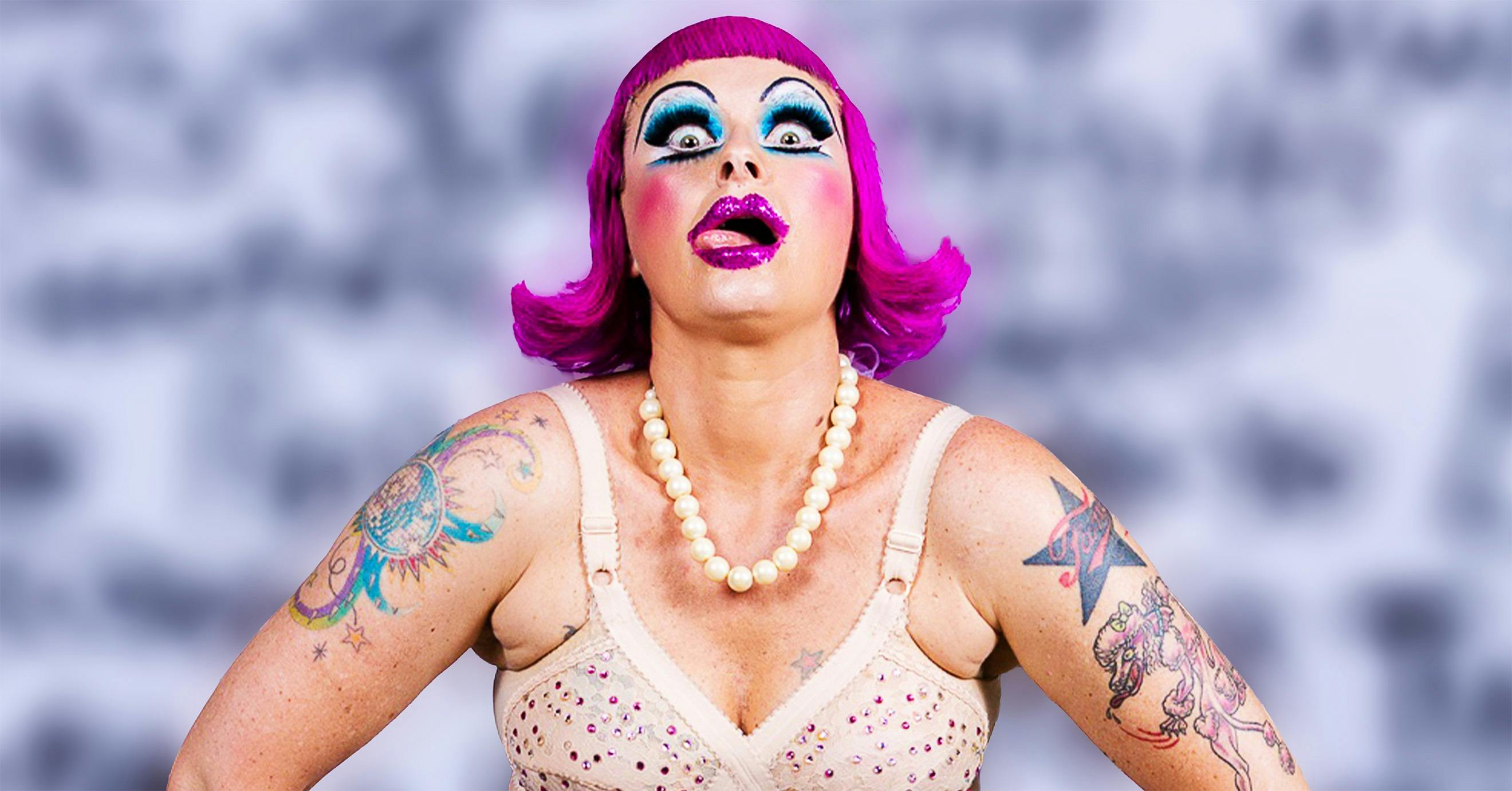 A woman performer wearing a fluro pink wig pulling a shocked expression at the camera