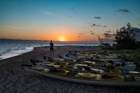 A person stands on Wheeler Island beach watching the sun set. The fleet of coral sea kayaks in fore