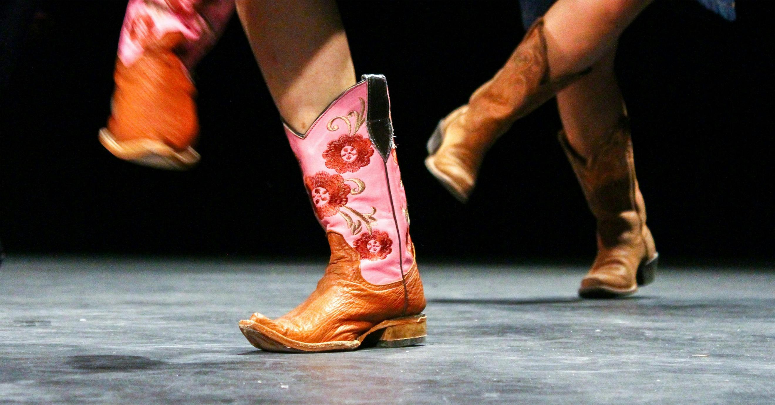 A close up on multiple people's feet wearing colourful cowboy boots dancing
