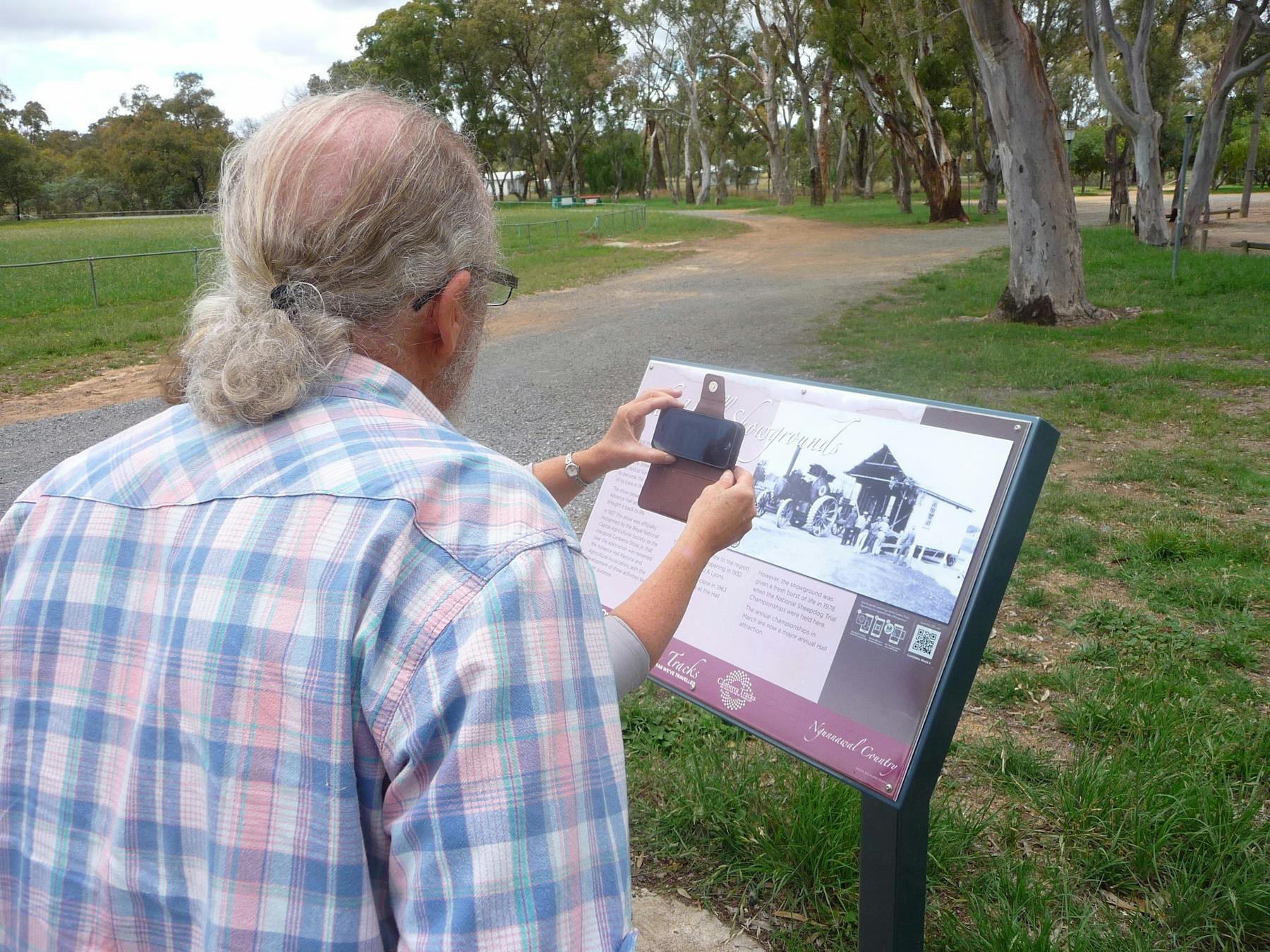 Back of man obstructing woman who has smartphone in front of sign