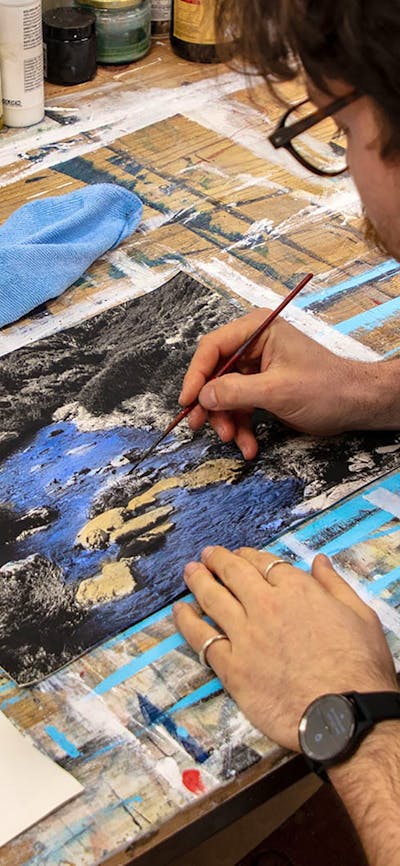 A photo of a man painting a black and white darkroom image of a river