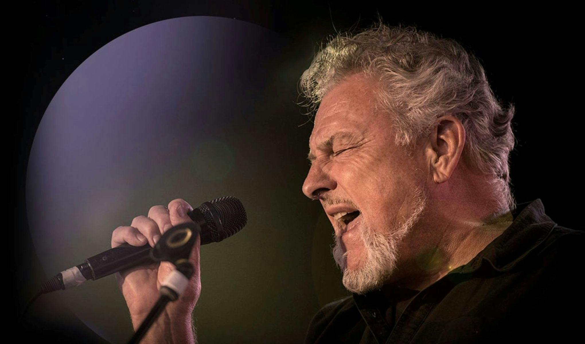 A man holding a microphone and singing with his eyes closed.