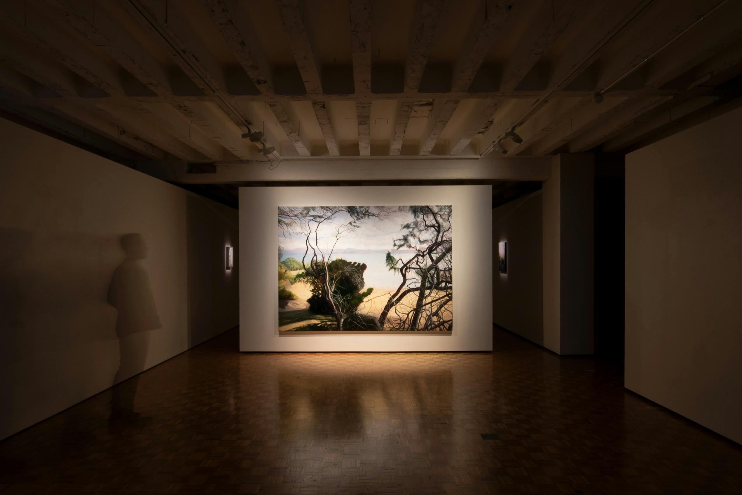 Gallery main room with a painting dramatically lit and featured on the back wall.