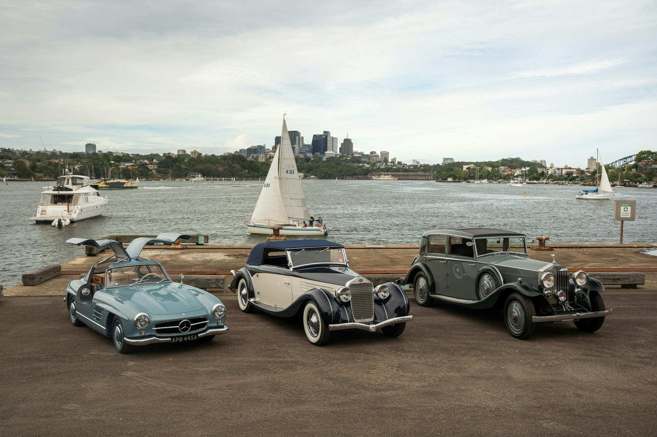 Three vintage cars parked on the Sydney harbour.