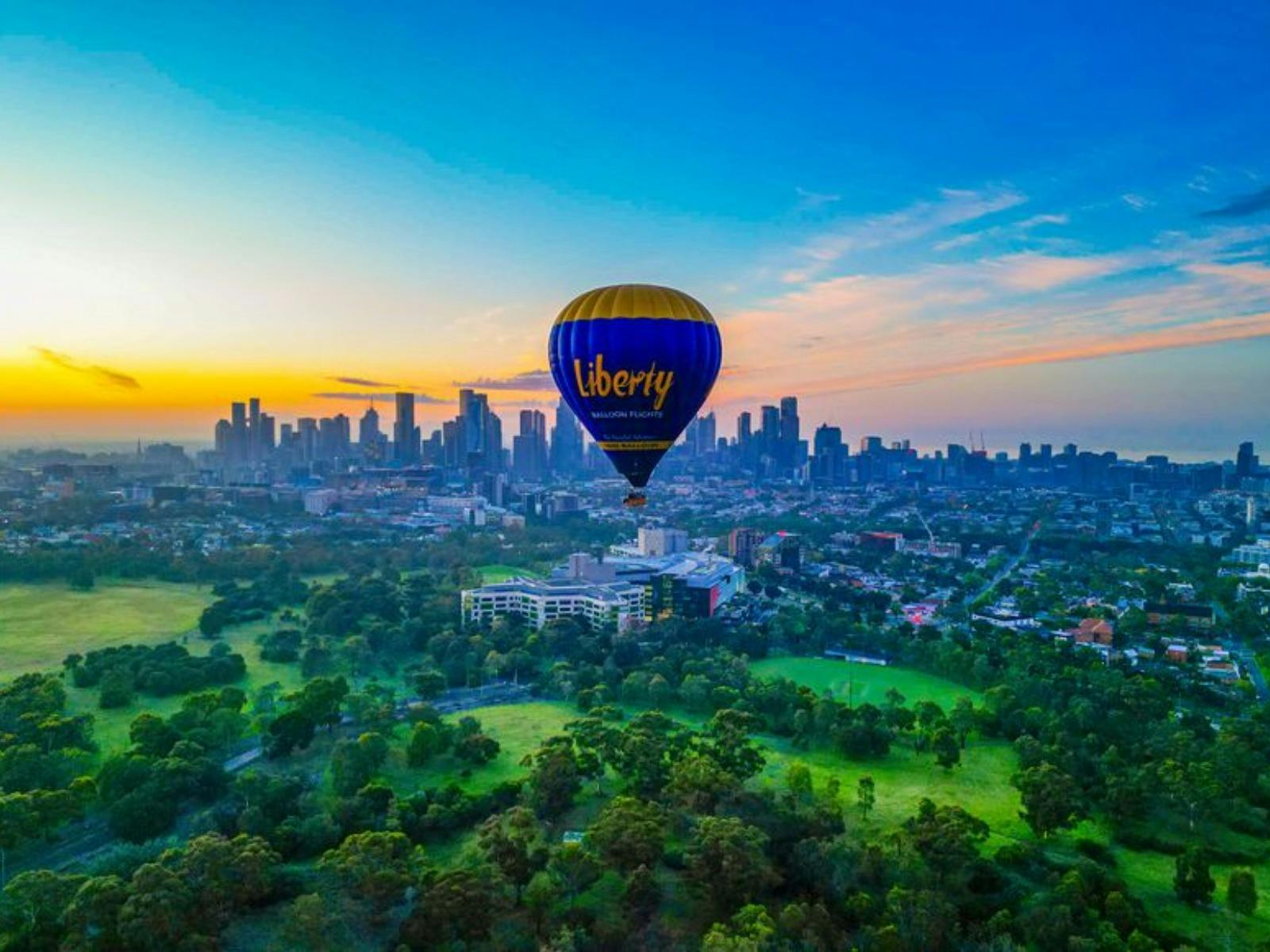 Hot air balloon floating above lush green parklands with city skyline in the background