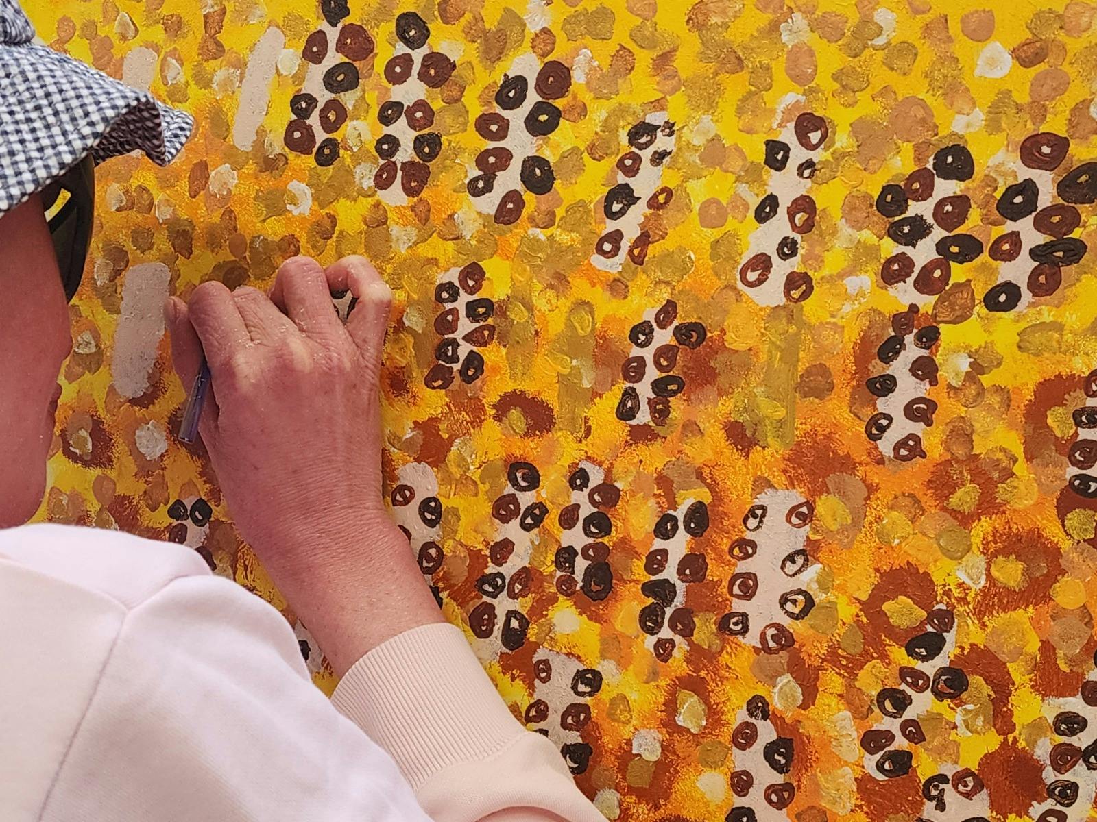 Artist from the Art Factory painting small dots onto yellow canvas.
