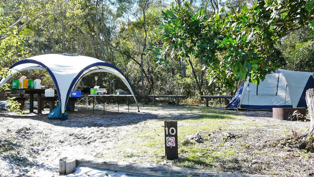 Blue tent set up beside a shaded picnic table.