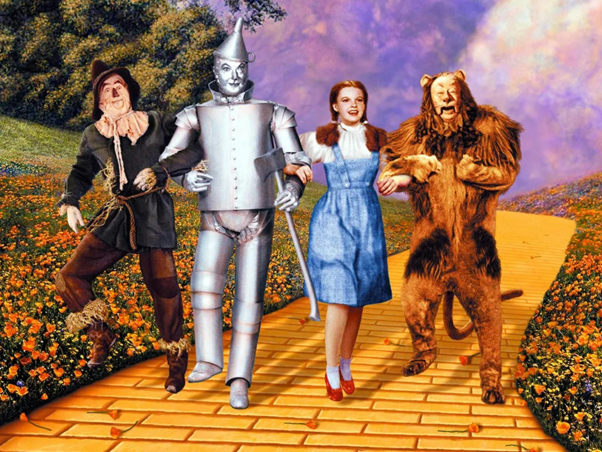 Still from The Wizard of Oz showing a scarecrow, tin man, woman and lion on a yellow brick road