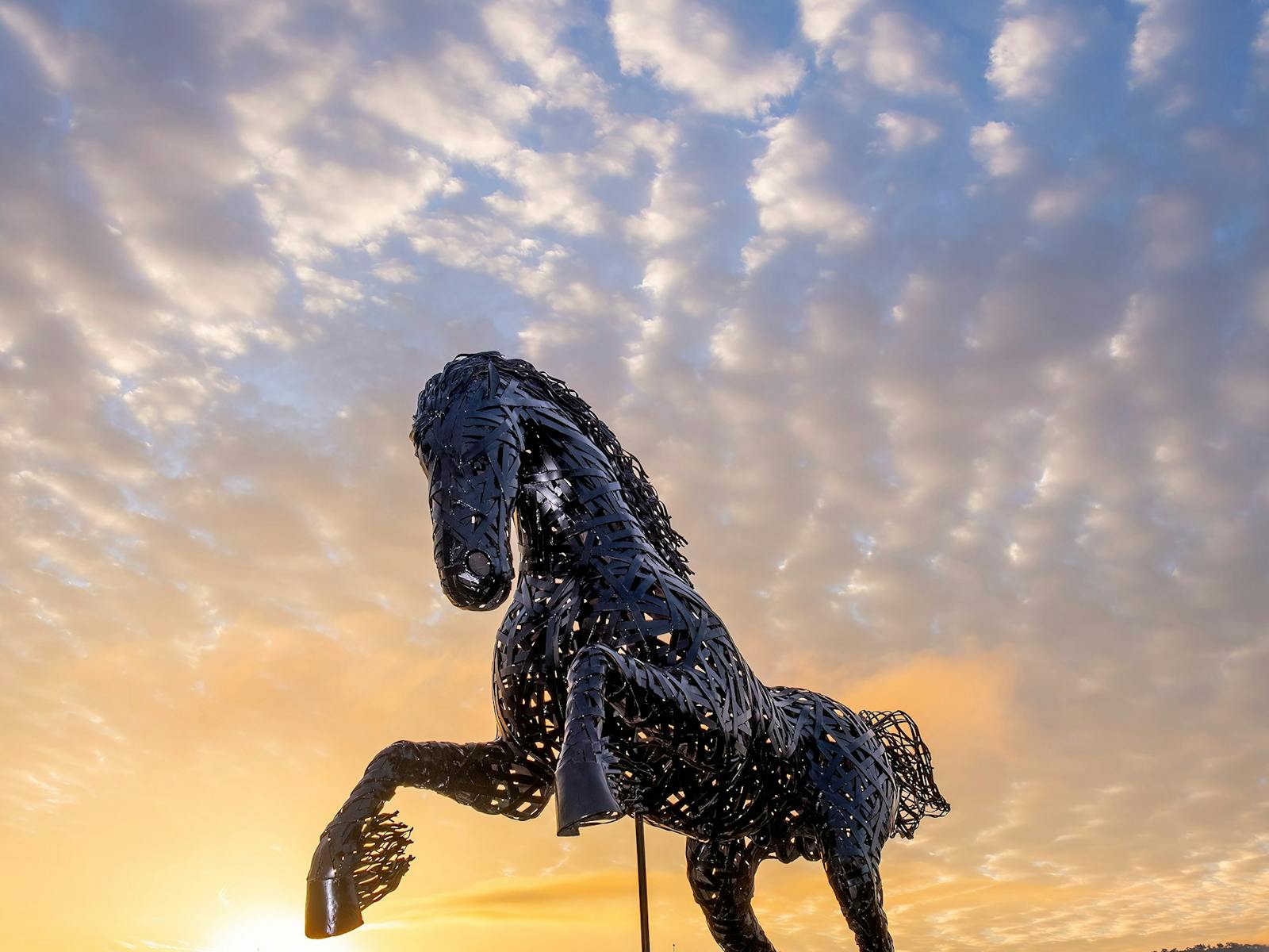A stunning metal horse rearing on its hindlegs, against a glowing sunset sky backdrop.