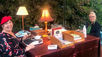 Two women sitting with typewriters and stationery