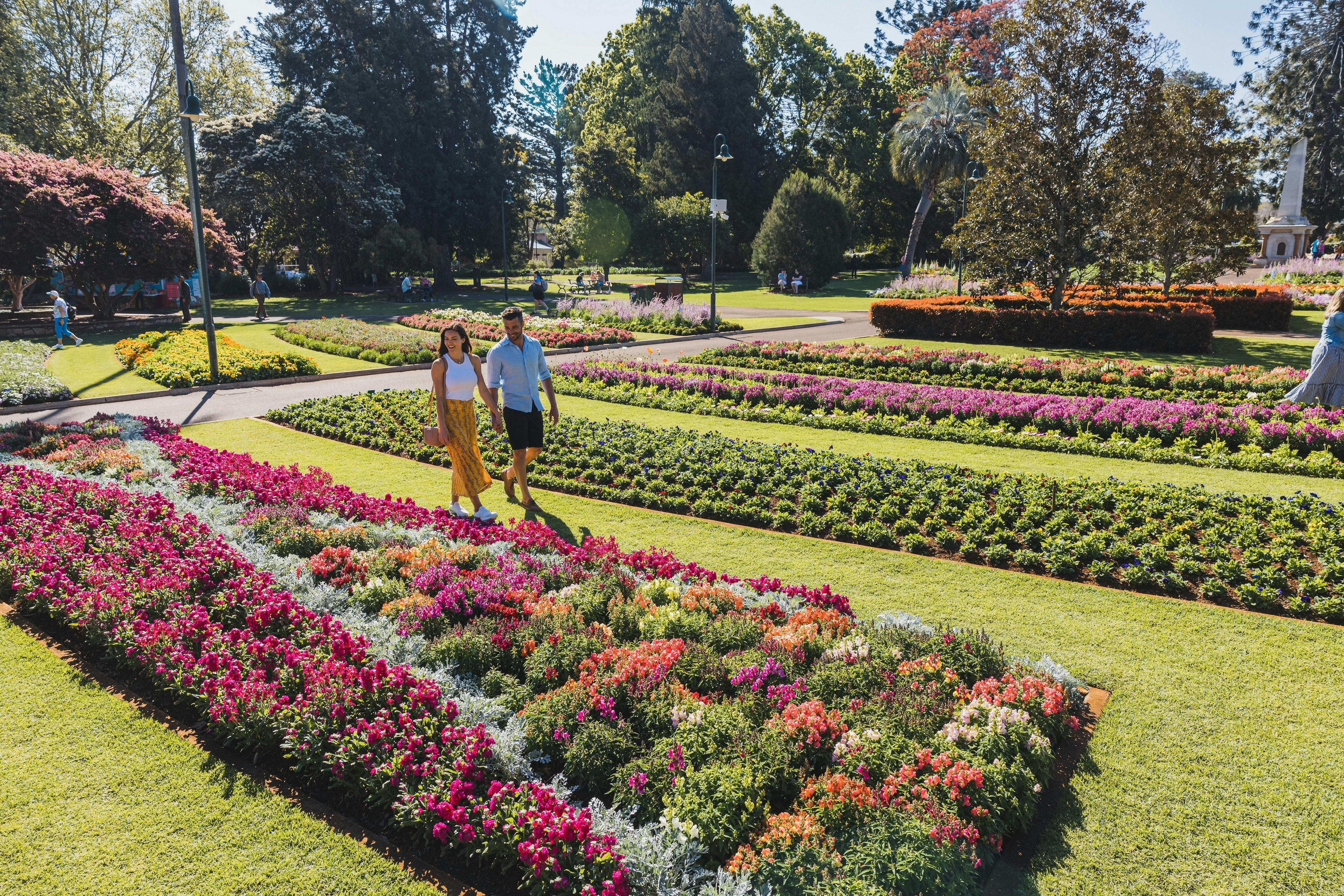 Couple walking in park next to blooming garden beds.