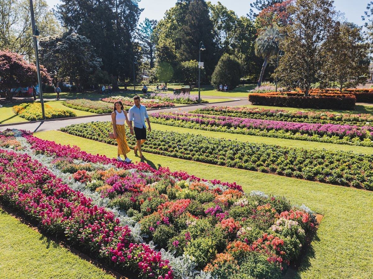 Couple walking in park next to blooming garden beds.