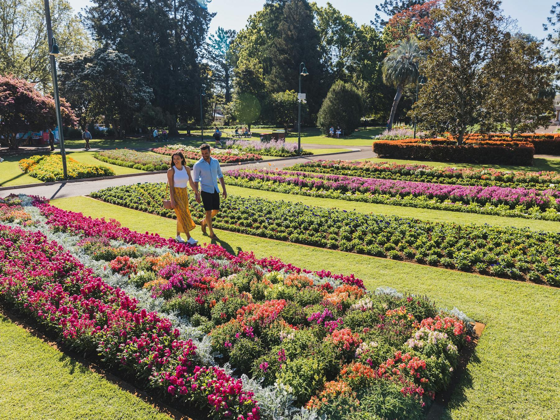 Couple walking in park next to blooming garden beds.